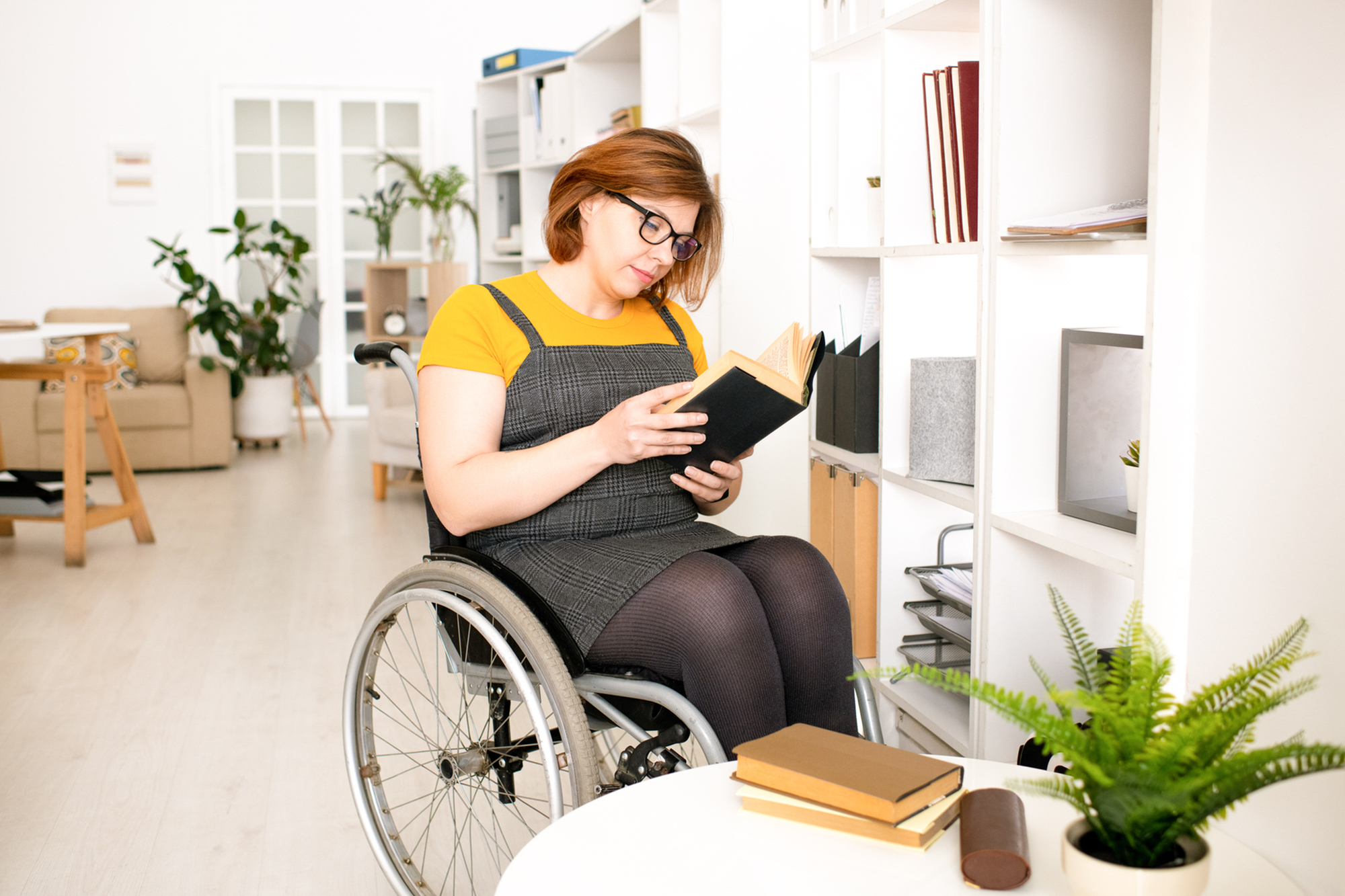 woman in a wheelchair reading a book on wood-style floors