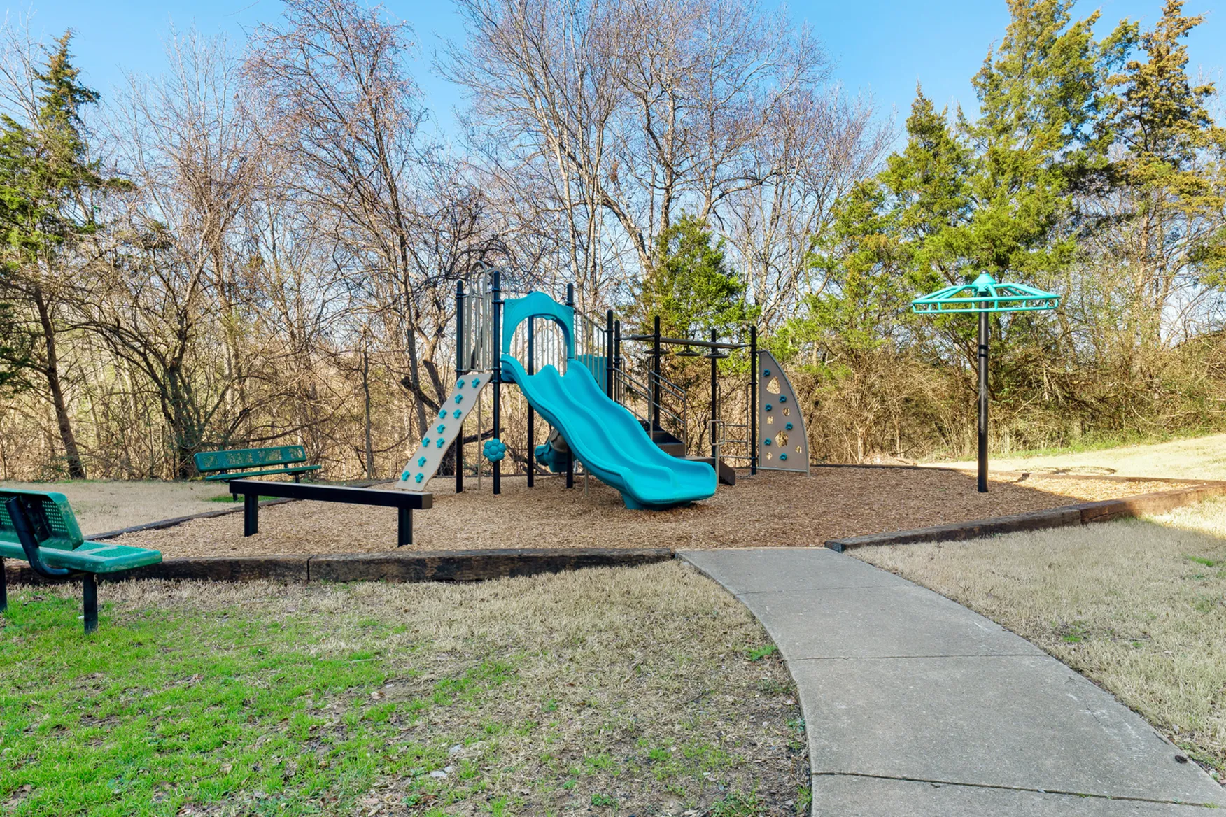 Inviting playground with vibrant blue slides and climbing structures surrounded by lush trees, perfect for family fun.
