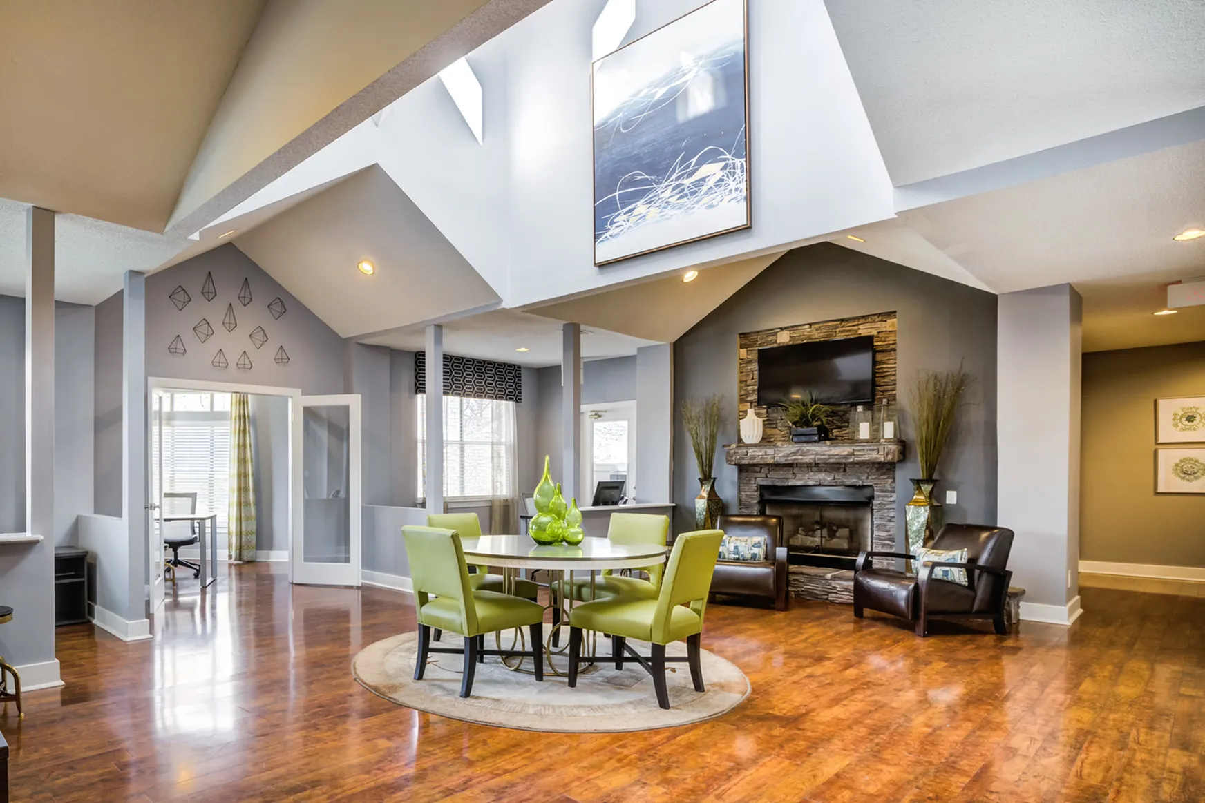 Elegant clubhouse with vaulted ceiling, modern fireplace, and stylish decor, featuring vibrant green chairs around a circular table on polished wood flooring.