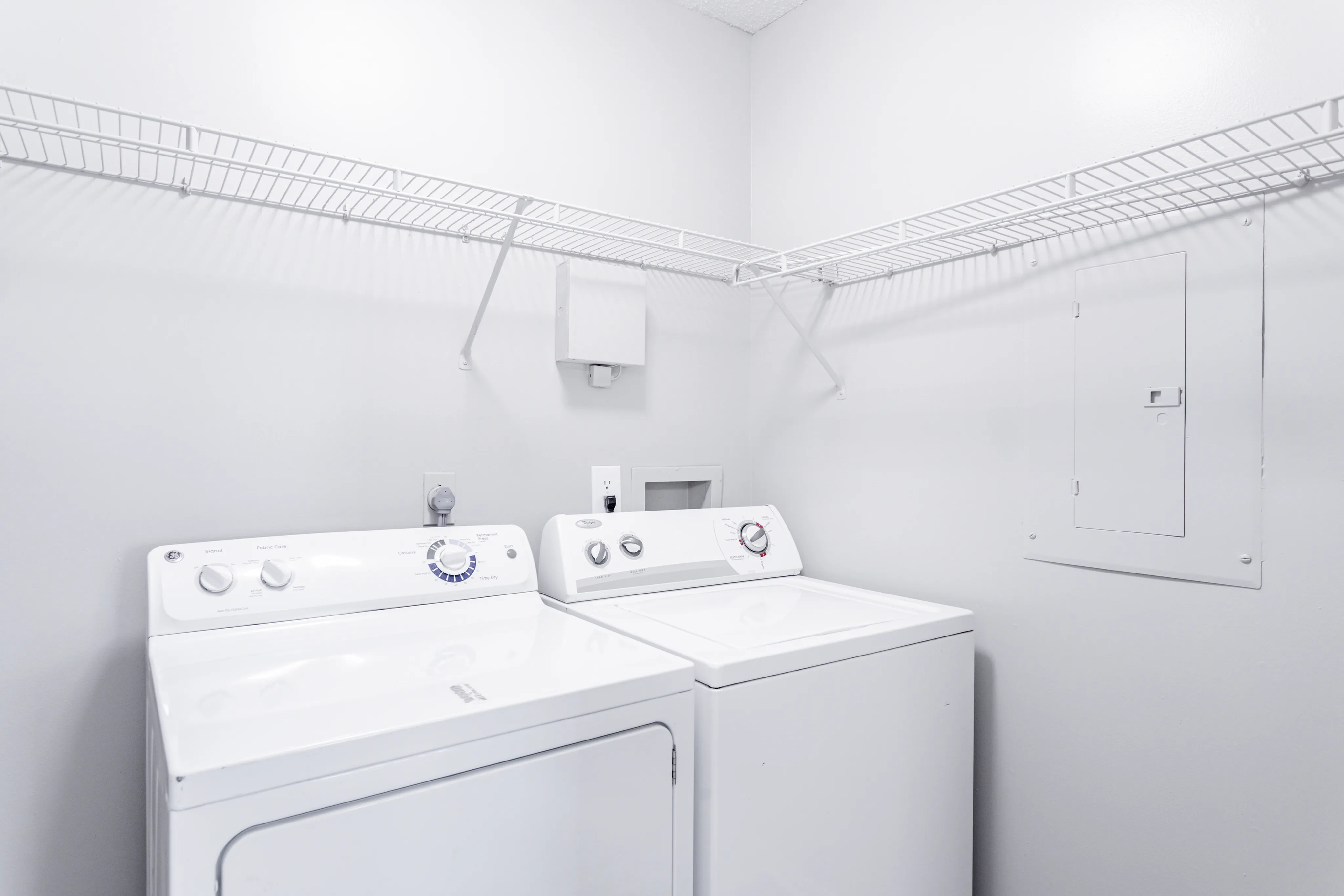 Modern laundry room with sleek white washer and dryer, featuring convenient overhead shelving for storage.