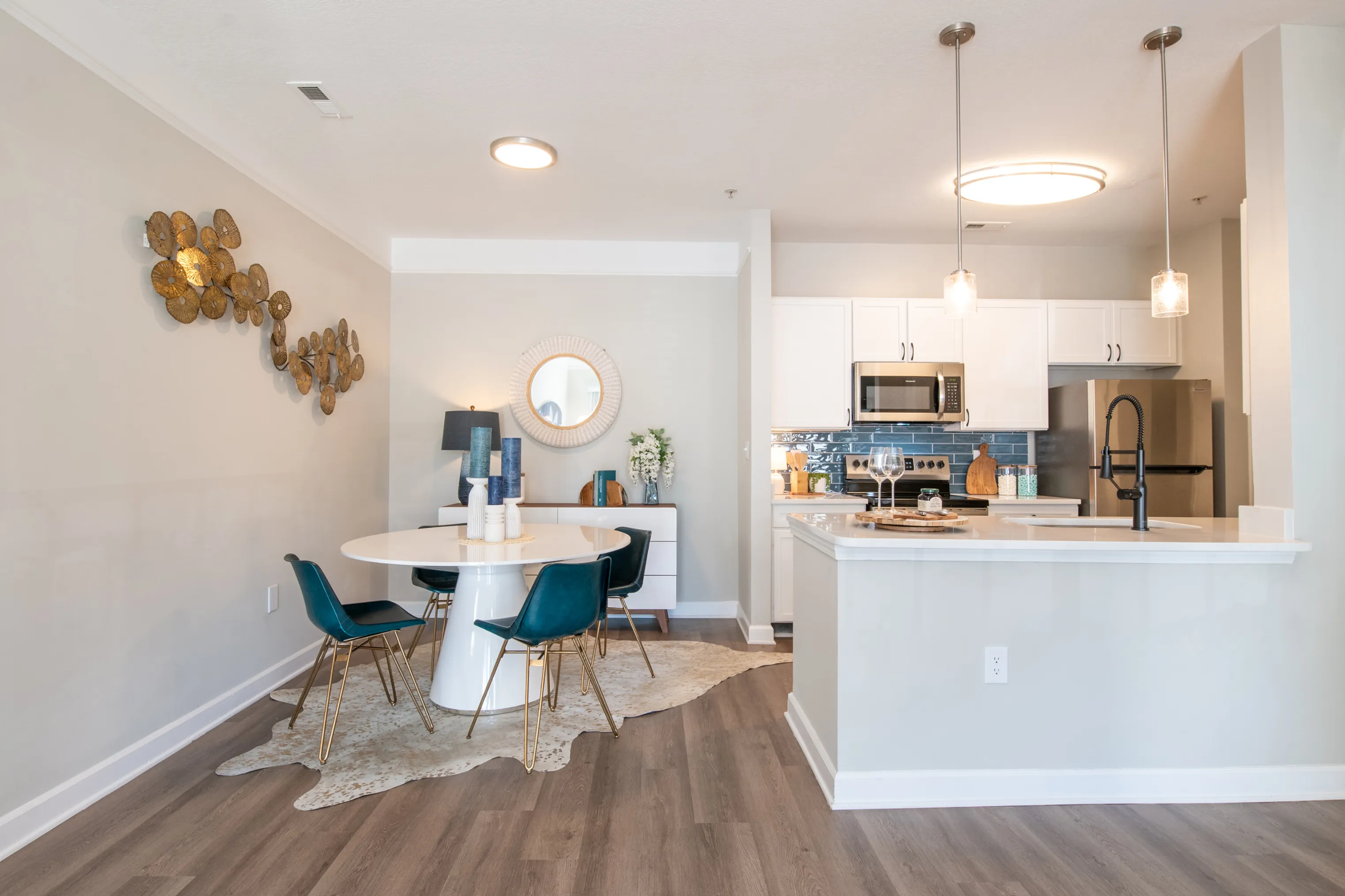 Chic apartment interior showcasing a modern kitchen with stainless steel appliances, elegant pendant lighting, and a stylish dining area with a unique round table and plush teal chairs.