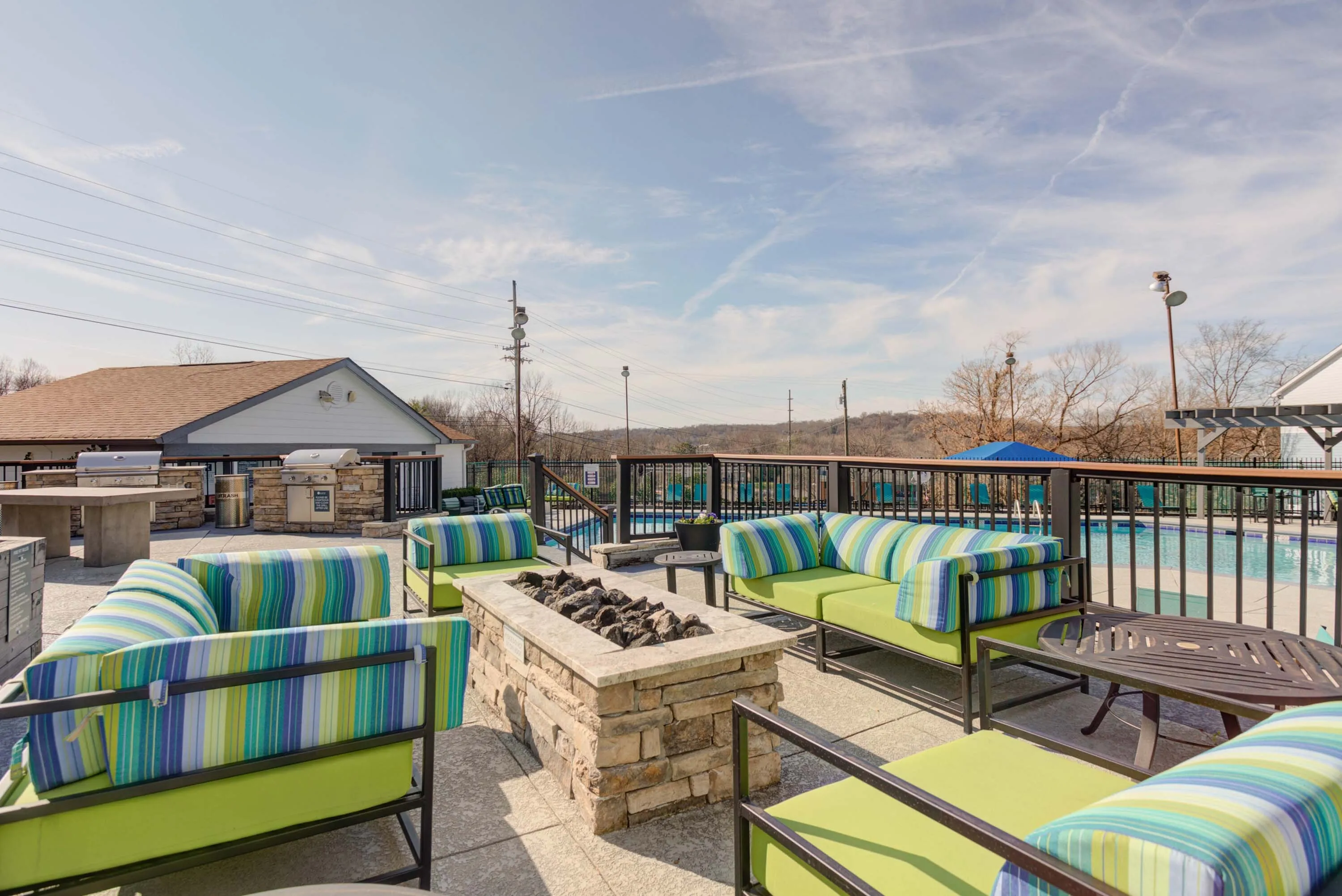 Inviting outdoor lounge area with vibrant seating and stone fire pit, overlooking a pristine swimming pool under a clear blue sky.