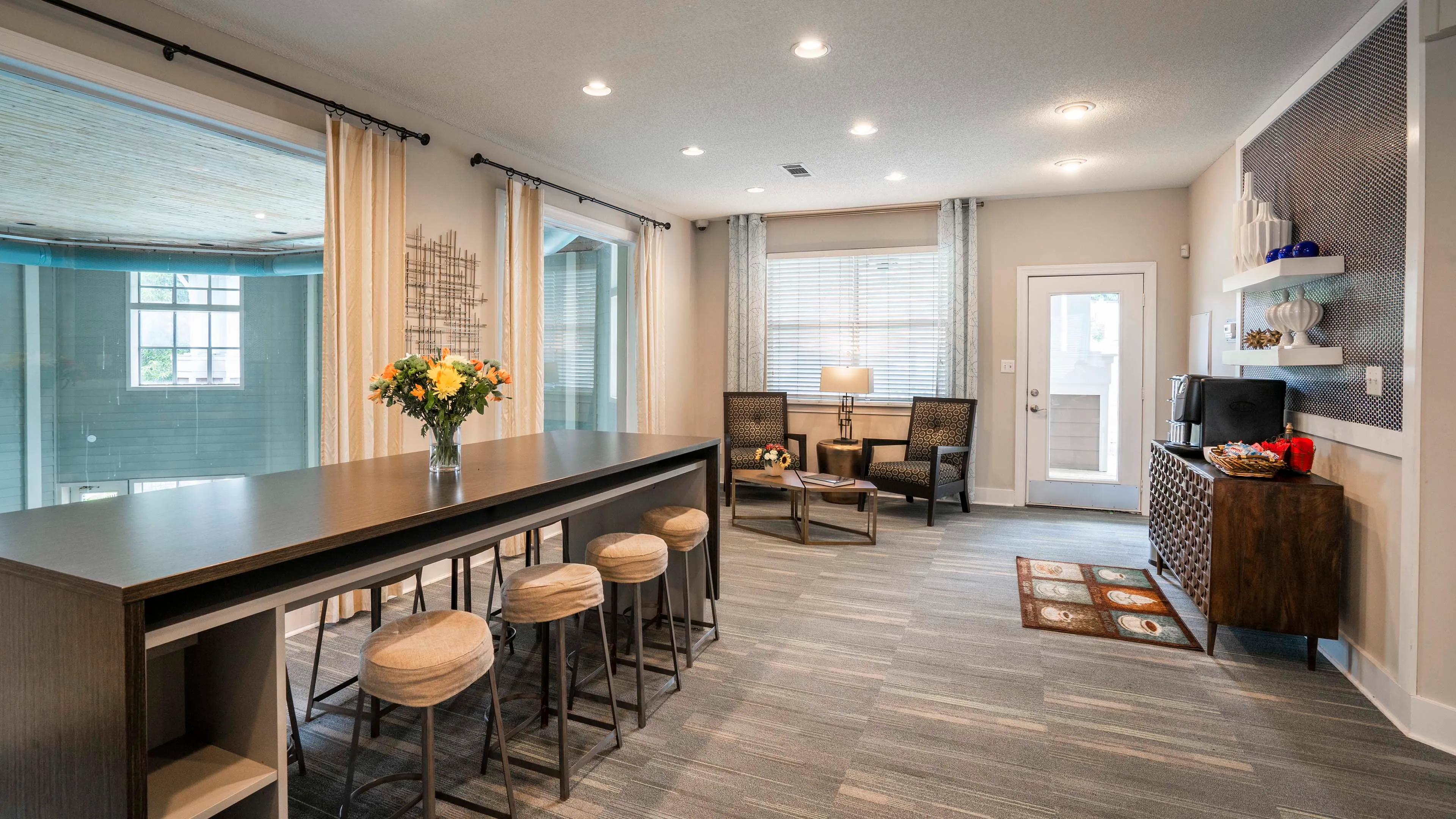 Inviting lounge area in modern apartment featuring a stylish high-top table with bar stools, cozy chairs by the window, and sleek decor.