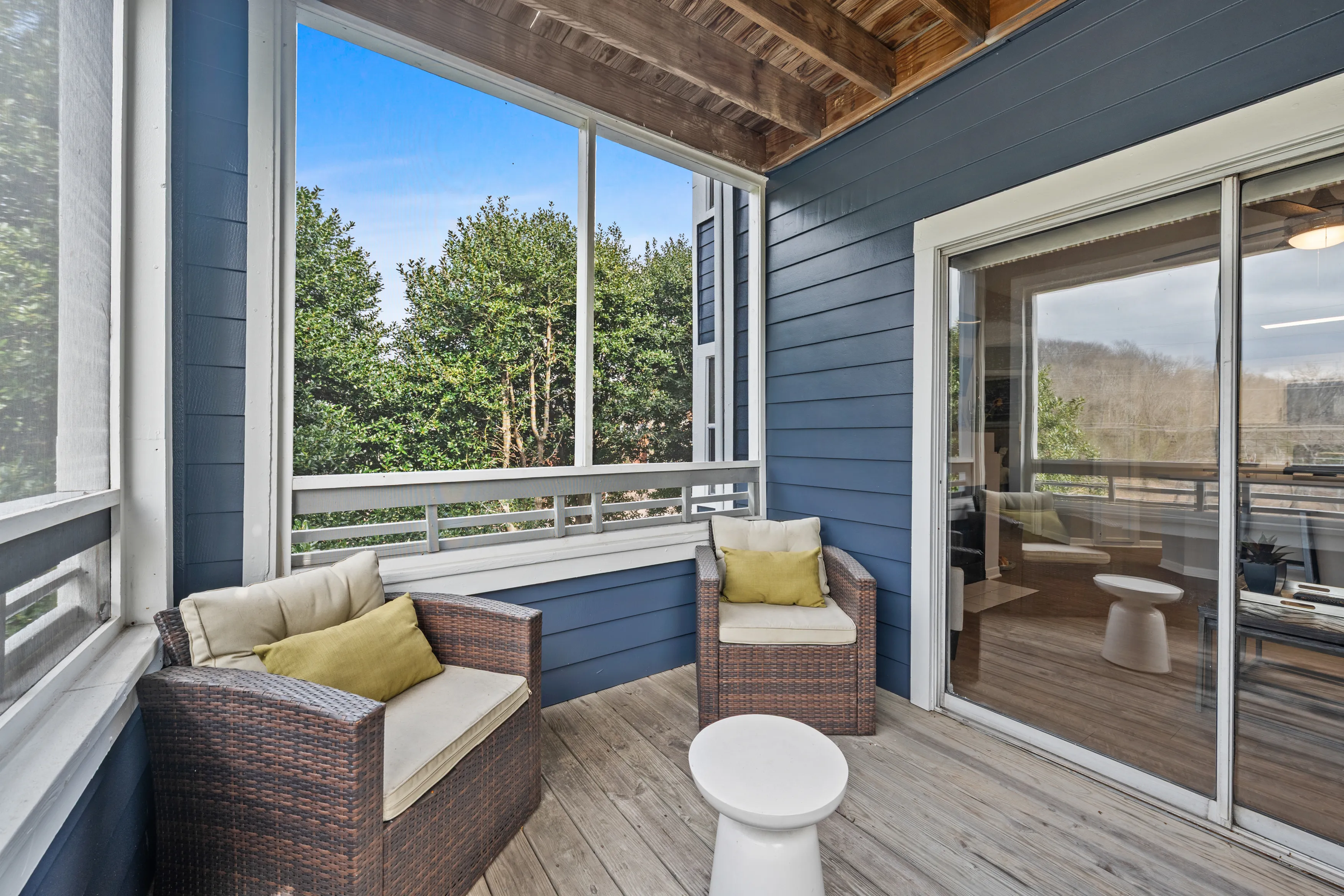 Charming screened porch with cozy wicker seating and lush greenery views, perfect for relaxing outdoors.