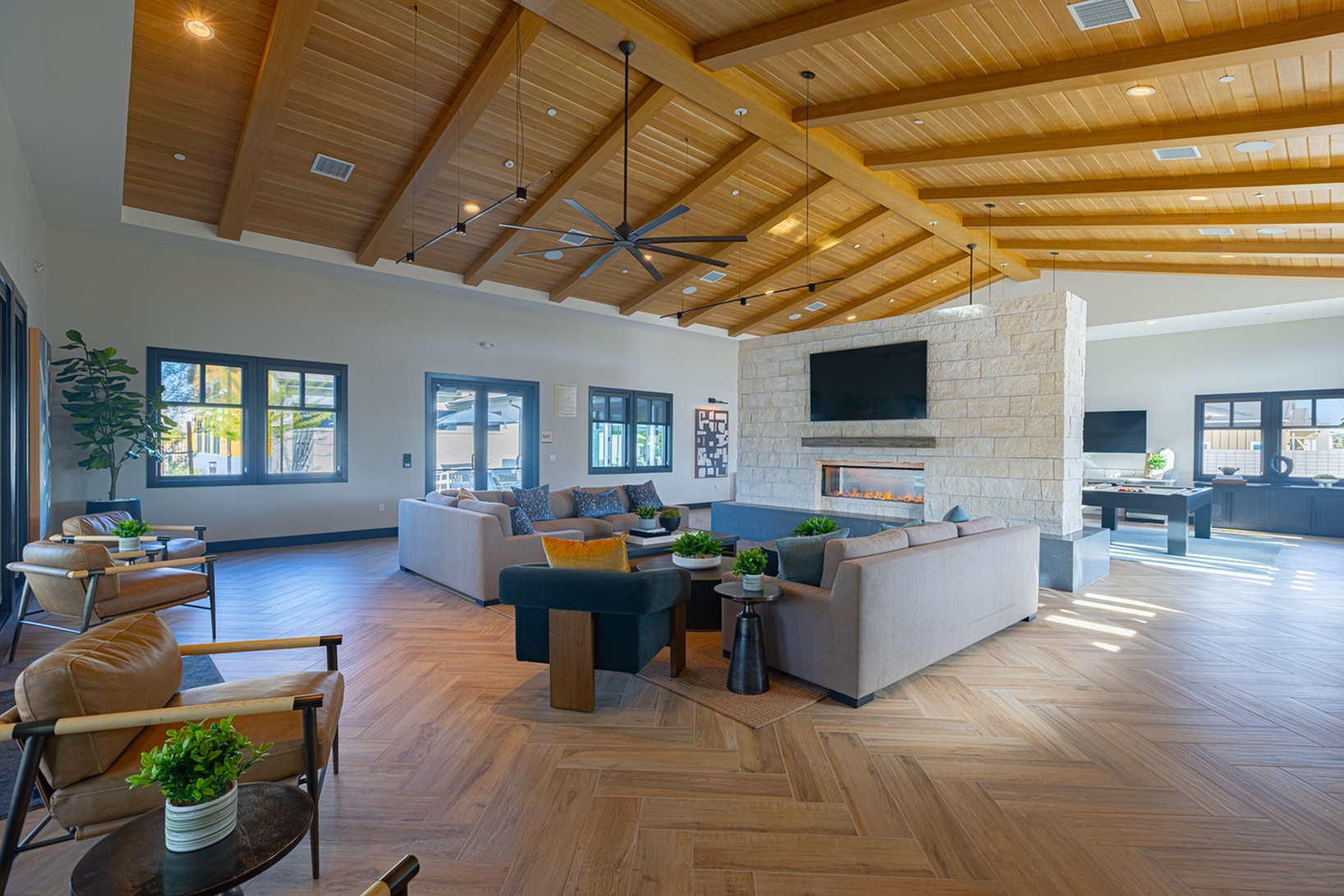 Spacious clubhouse area with vaulted wood ceilings, elegant stone fireplace, and modern decor, offering a warm and inviting atmosphere.