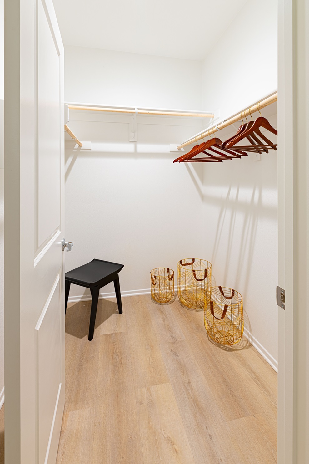 Modern and spacious oversized closet with light wooden floors, featuring elegant wooden hangers and stylish yellow storage baskets.