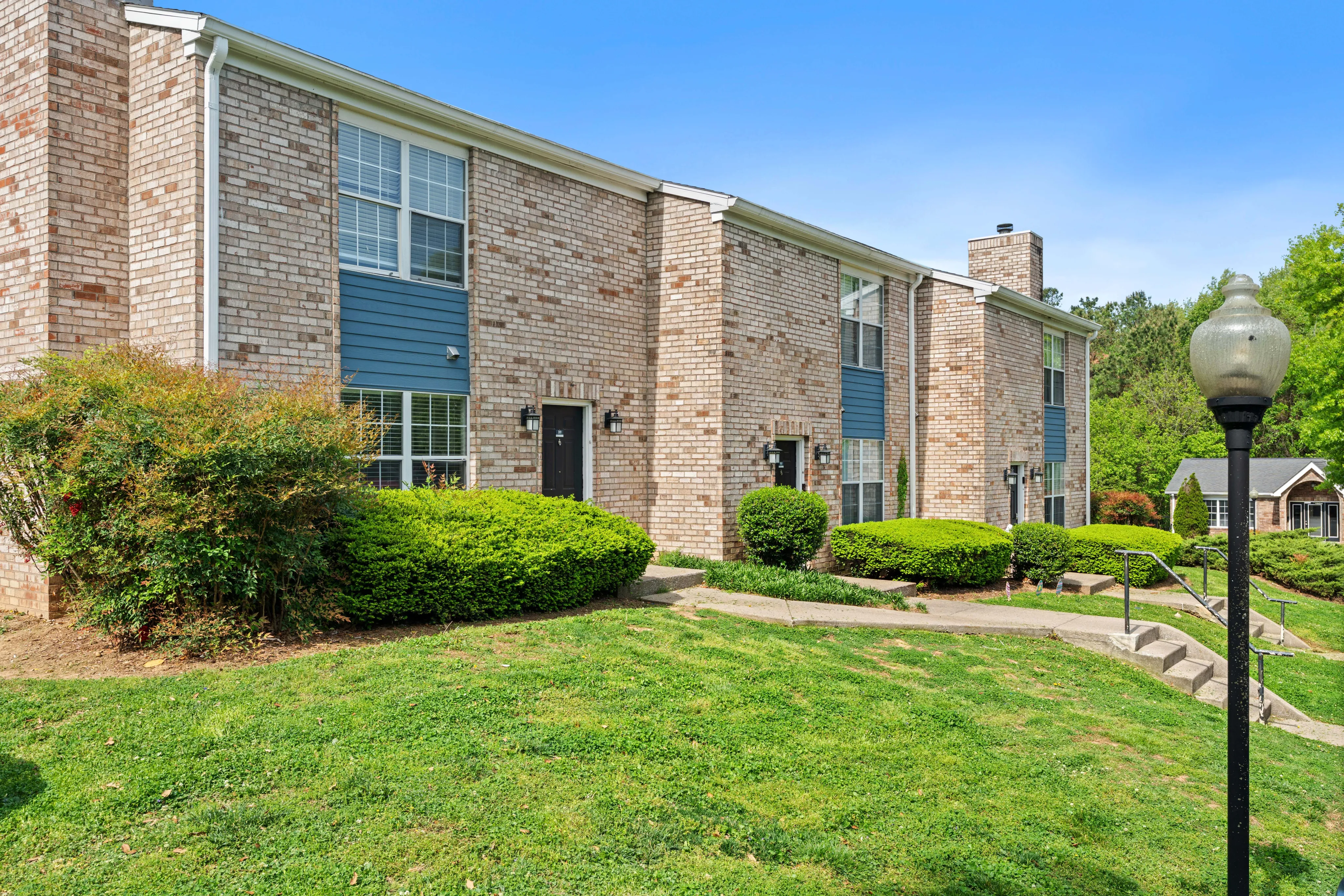 Charming brick apartment building with lush greenery and a peaceful walkway, offering a serene residential feel.