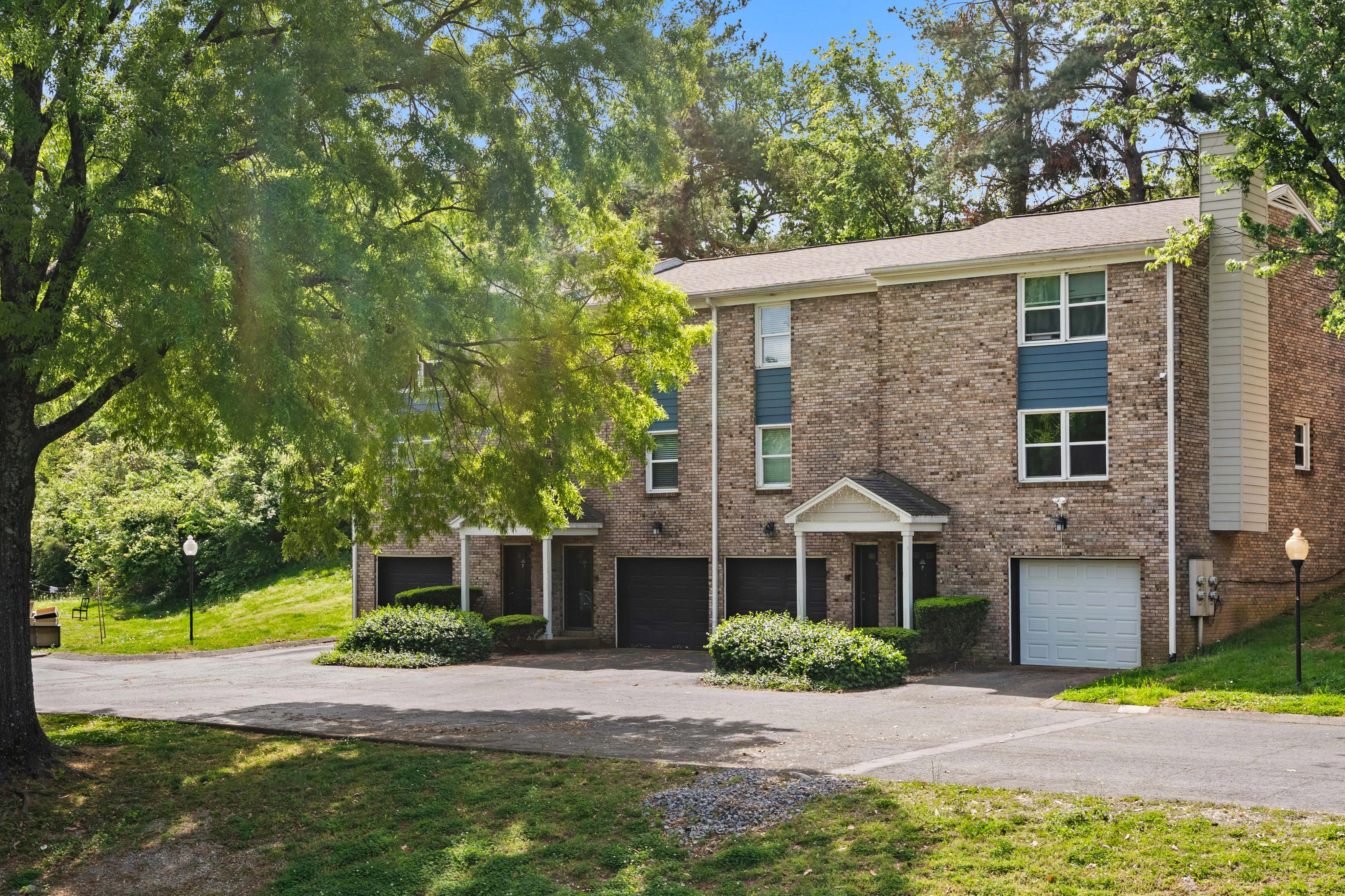 Inviting multi-story brick townhomes surrounded by lush greenery, featuring spacious garages and charming facades.