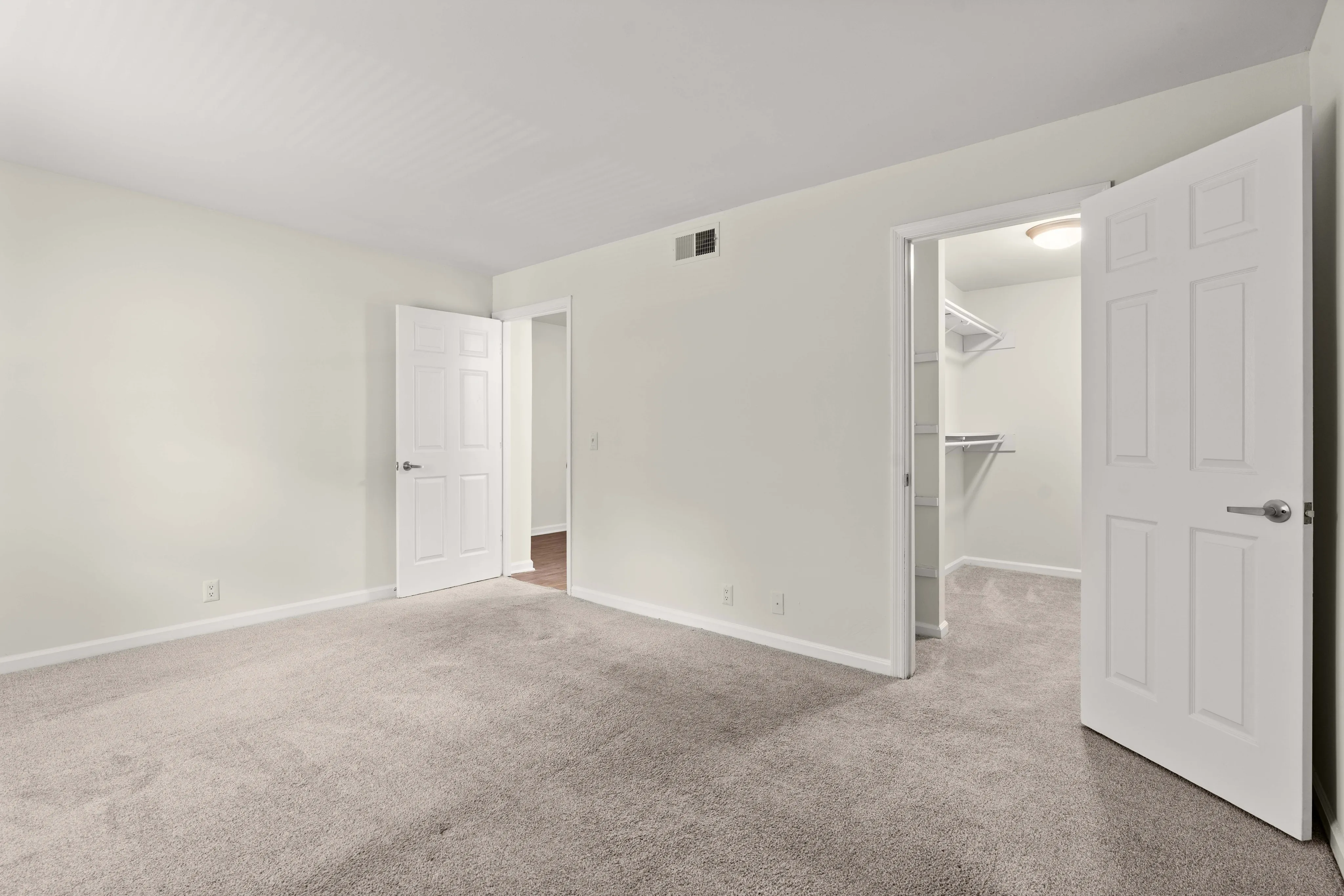 Spacious bedroom with plush carpeting, featuring an open walk-in closet and modern white doors.