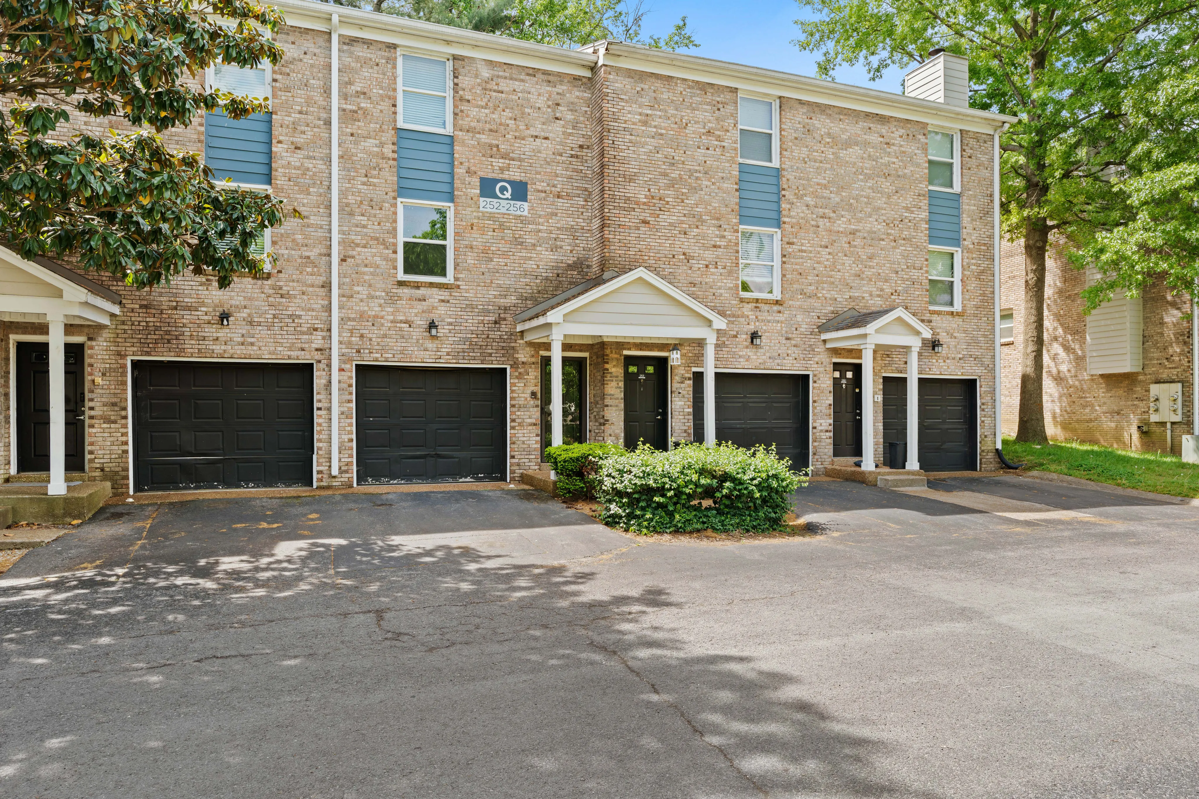 Charming brick townhouse with classic architecture, featuring three black garage doors and lush greenery, perfect for comfortable modern living.