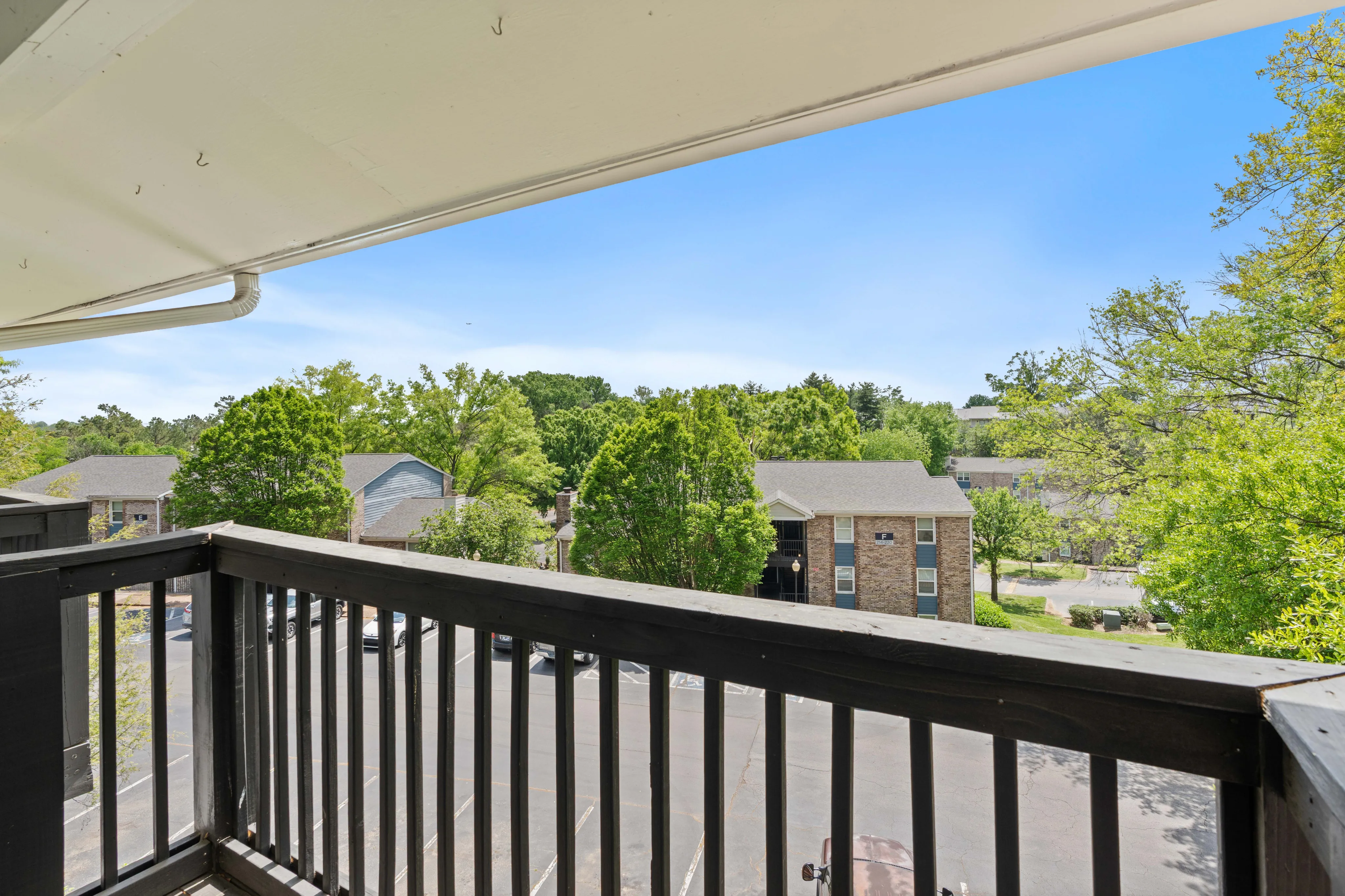Charming balcony view overlooking a lush, green neighborhood with clear blue skies and inviting residential surroundings.