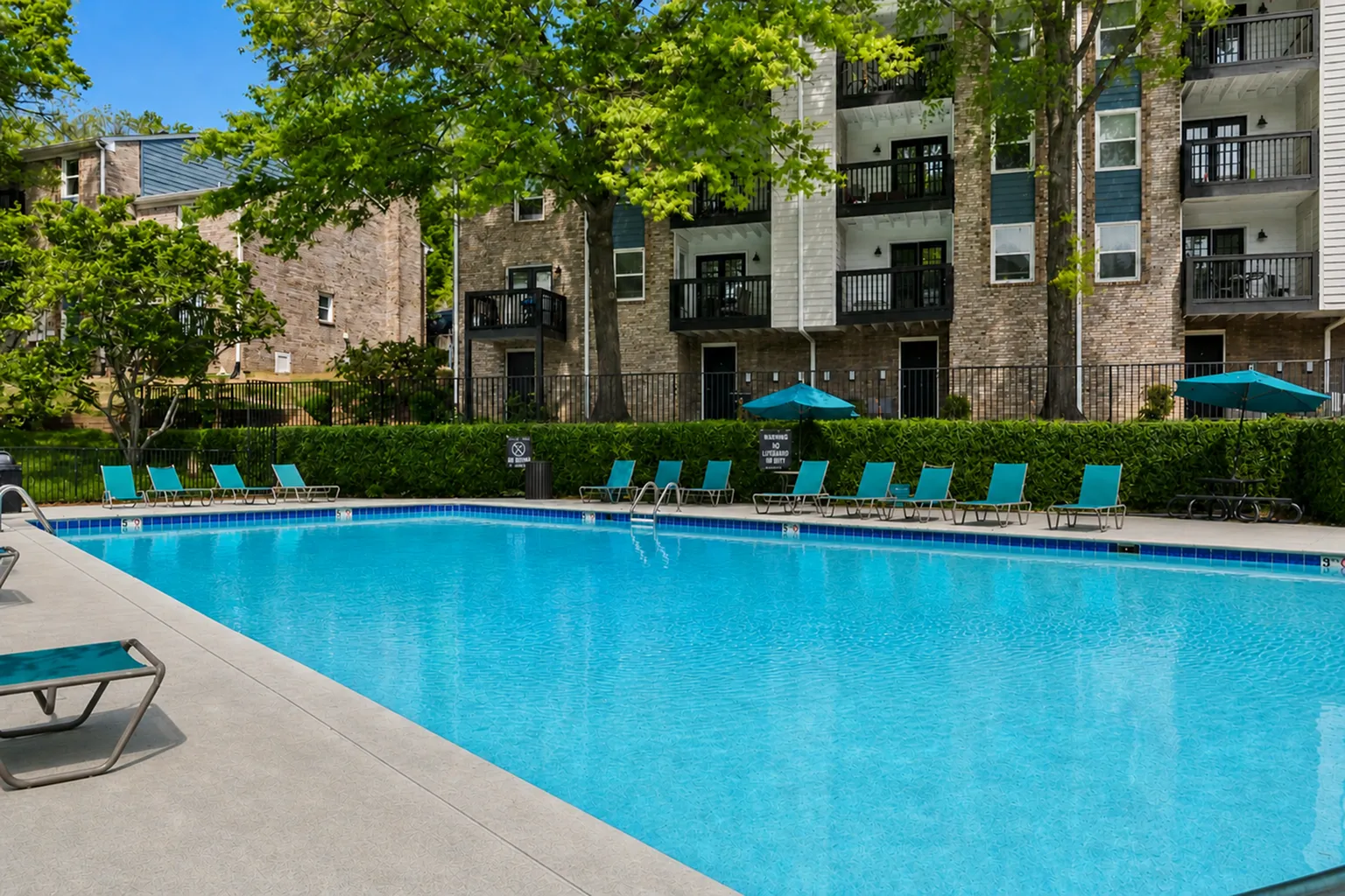 Captivating outdoor pool area surrounded by lush greenery and modern apartment buildings, featuring inviting lounge chairs and umbrellas for ultimate relaxation.