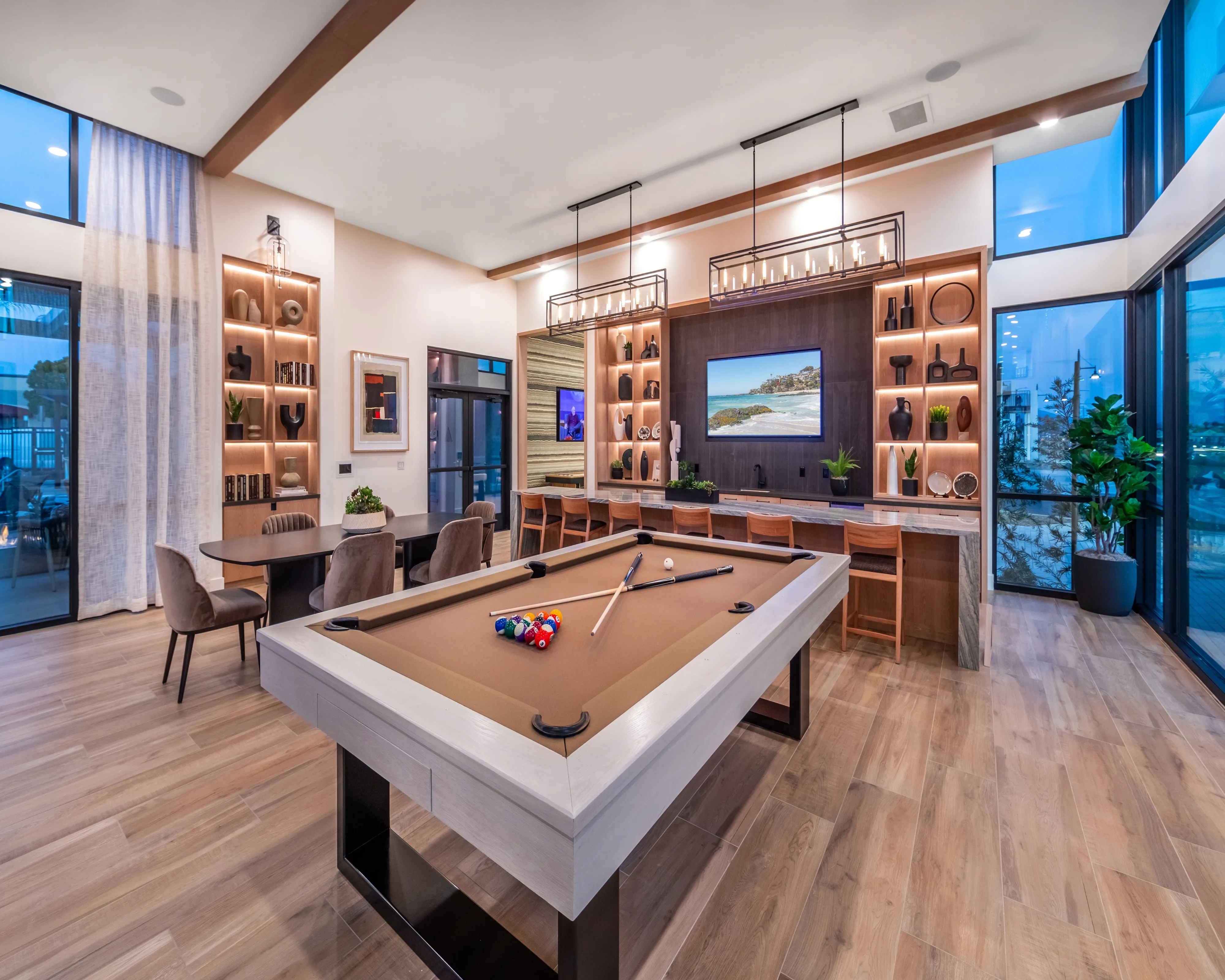 Modern clubroom with a sleek billiards table, stylish seating area, and ambient lighting. Features floor-to-ceiling windows and contemporary decor, perfect for entertaining and relaxation.