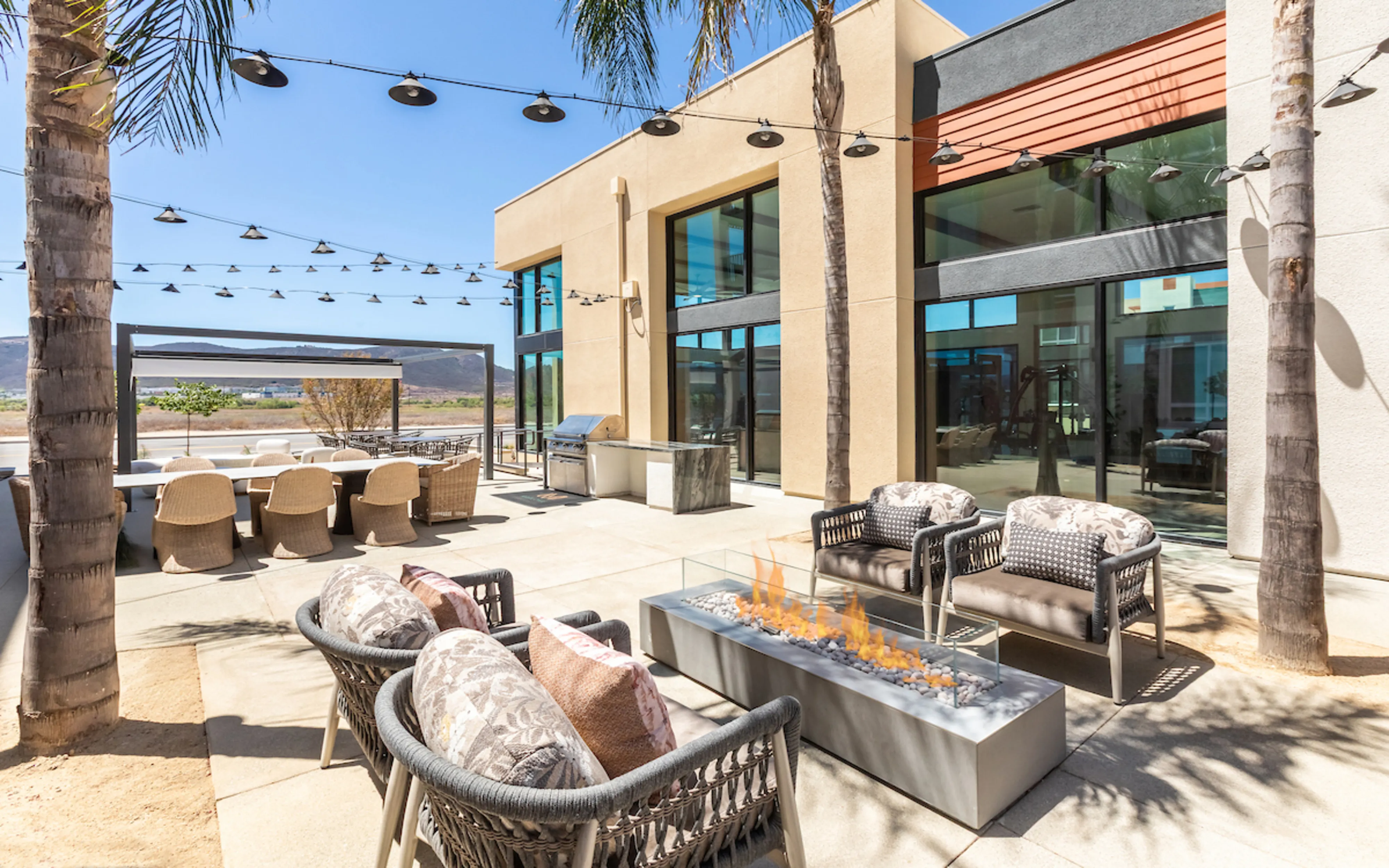 Luxurious outdoor patio with cozy seating, a modern fire pit, and sleek barbecue area, surrounded by tropical palms and stunning mountain views.