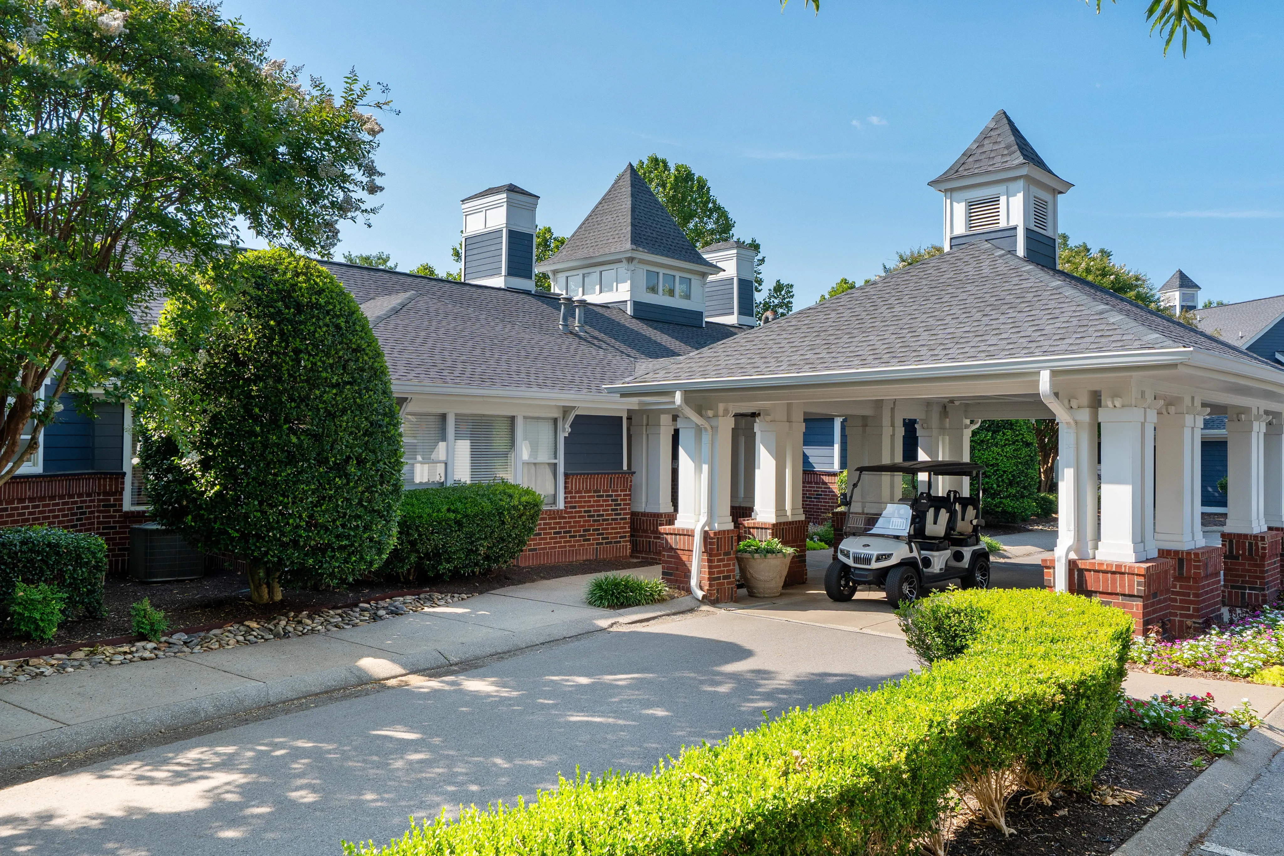 Charming residential entrance with elegant architecture, manicured shrubs, and a golf cart under a covered driveway.