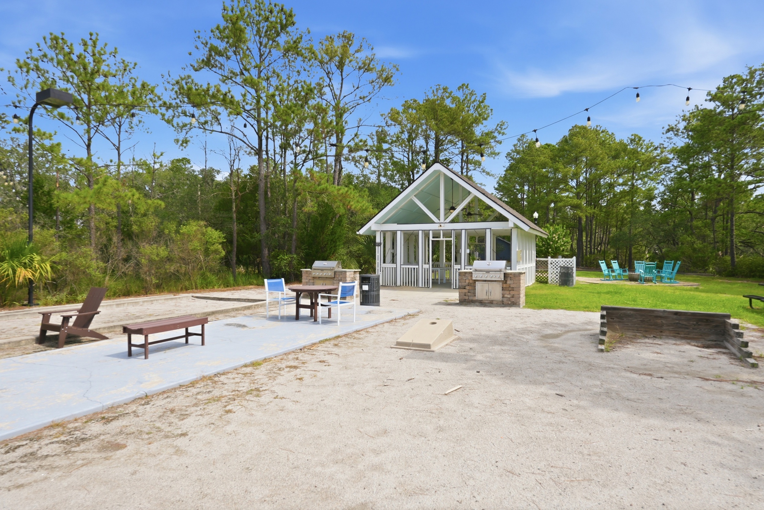Charming outdoor area featuring a cozy gazebo, picnic tables, and barbecue grills set amidst lush greenery and tall trees.