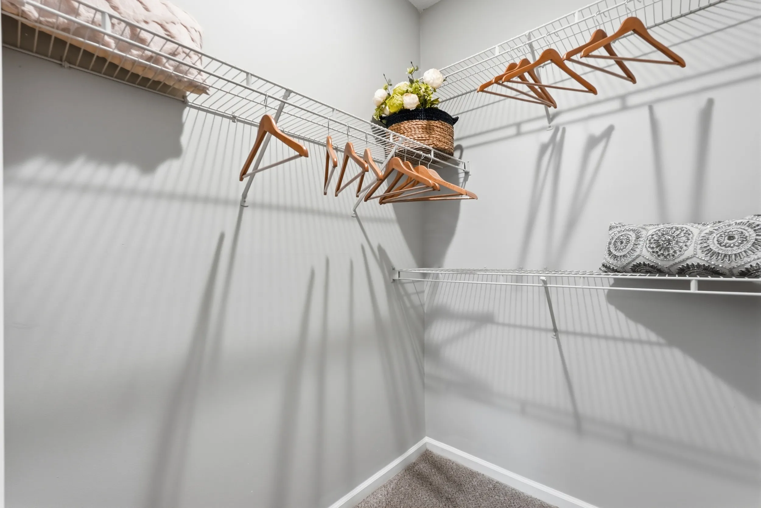 Spacious walk-in closet with sleek white wire shelving, elegant wood hangers, and decorative elements.