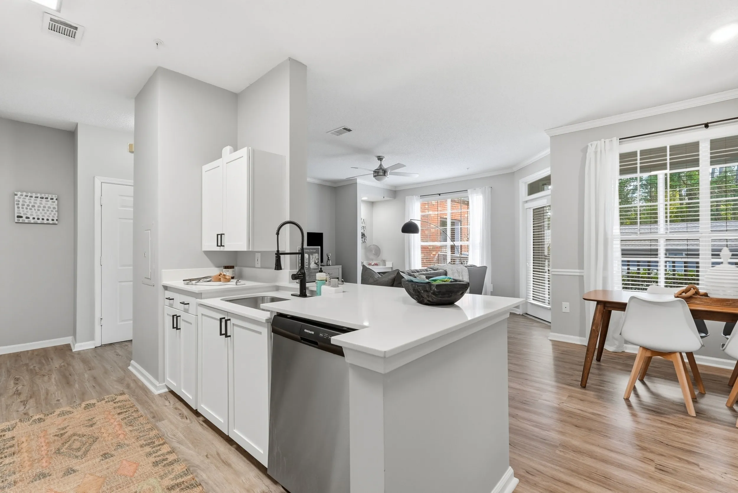 Modern open-concept kitchen with white cabinetry and stainless steel appliances, leading into a bright living area with large windows and elegant dining space.