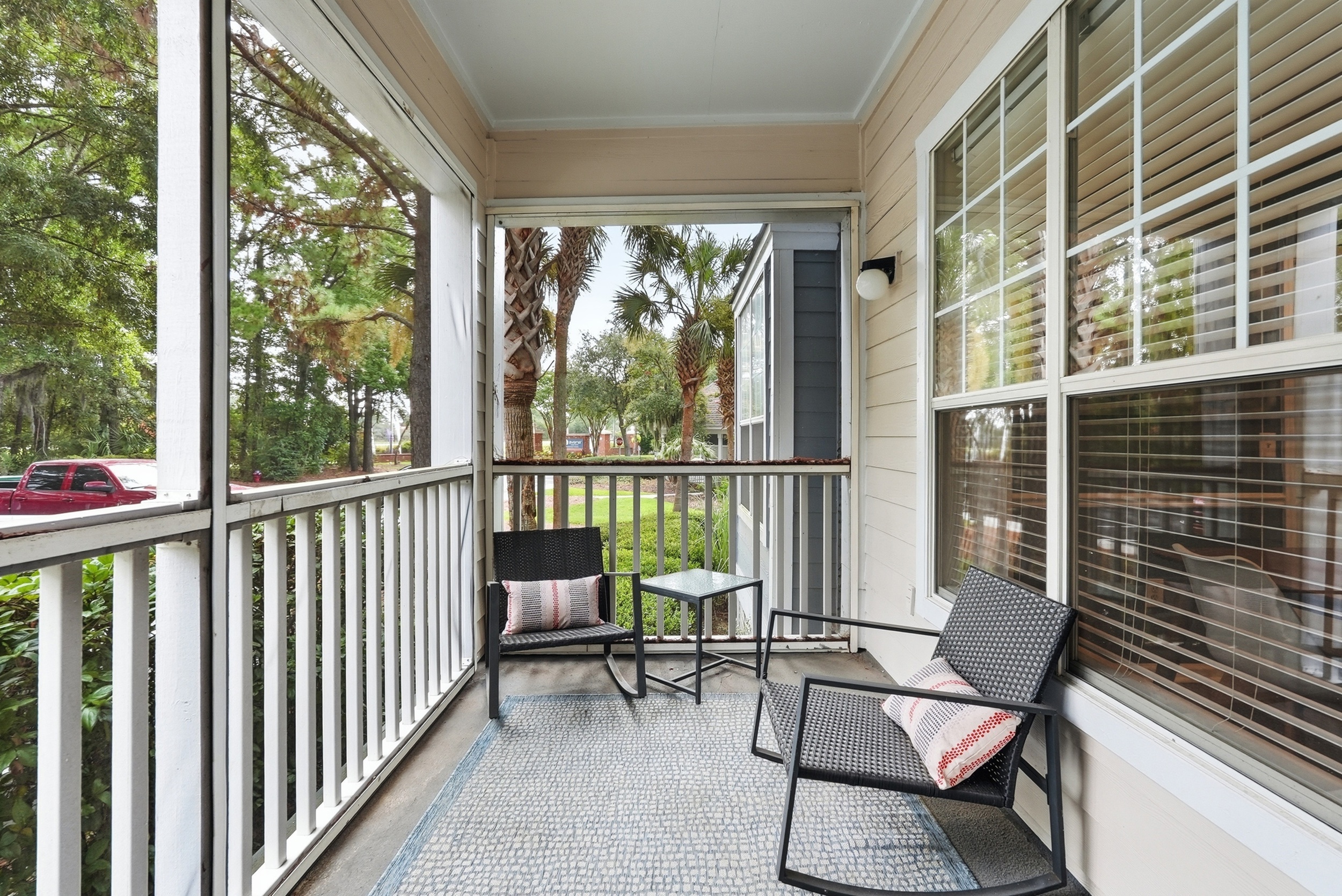 Charming screened-in balcony with cozy seating and scenic views of lush greenery, perfect for relaxation.