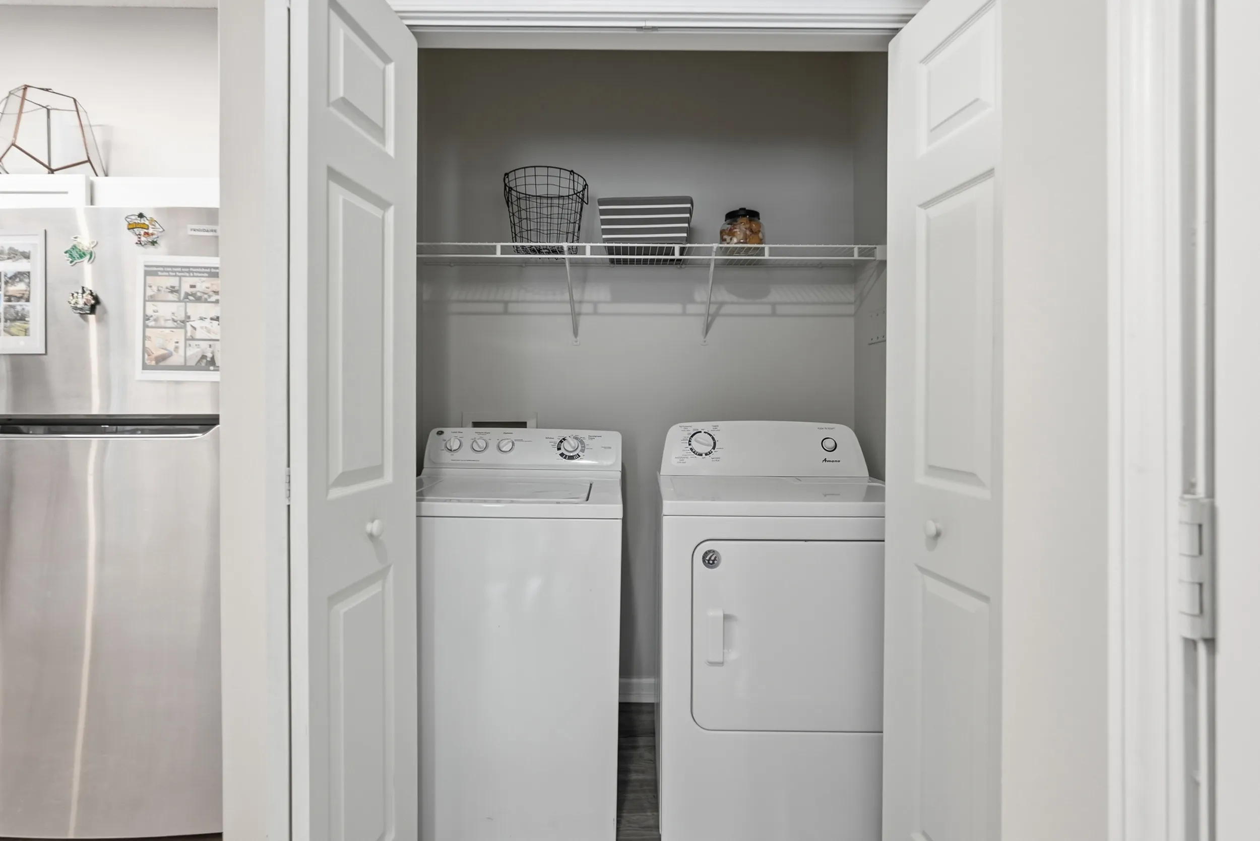Modern apartment laundry area featuring sleek washer and dryer with ample shelving space, conveniently nestled beside a stylish stainless steel refrigerator.