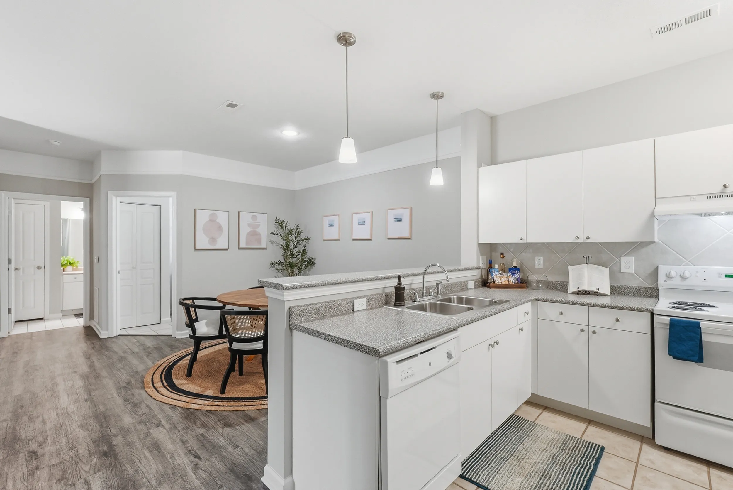 Modern kitchen and dining area with sleek white cabinetry, stainless steel sink, and cozy round dining table. Contemporary artwork and stylish lighting enhance the bright space.