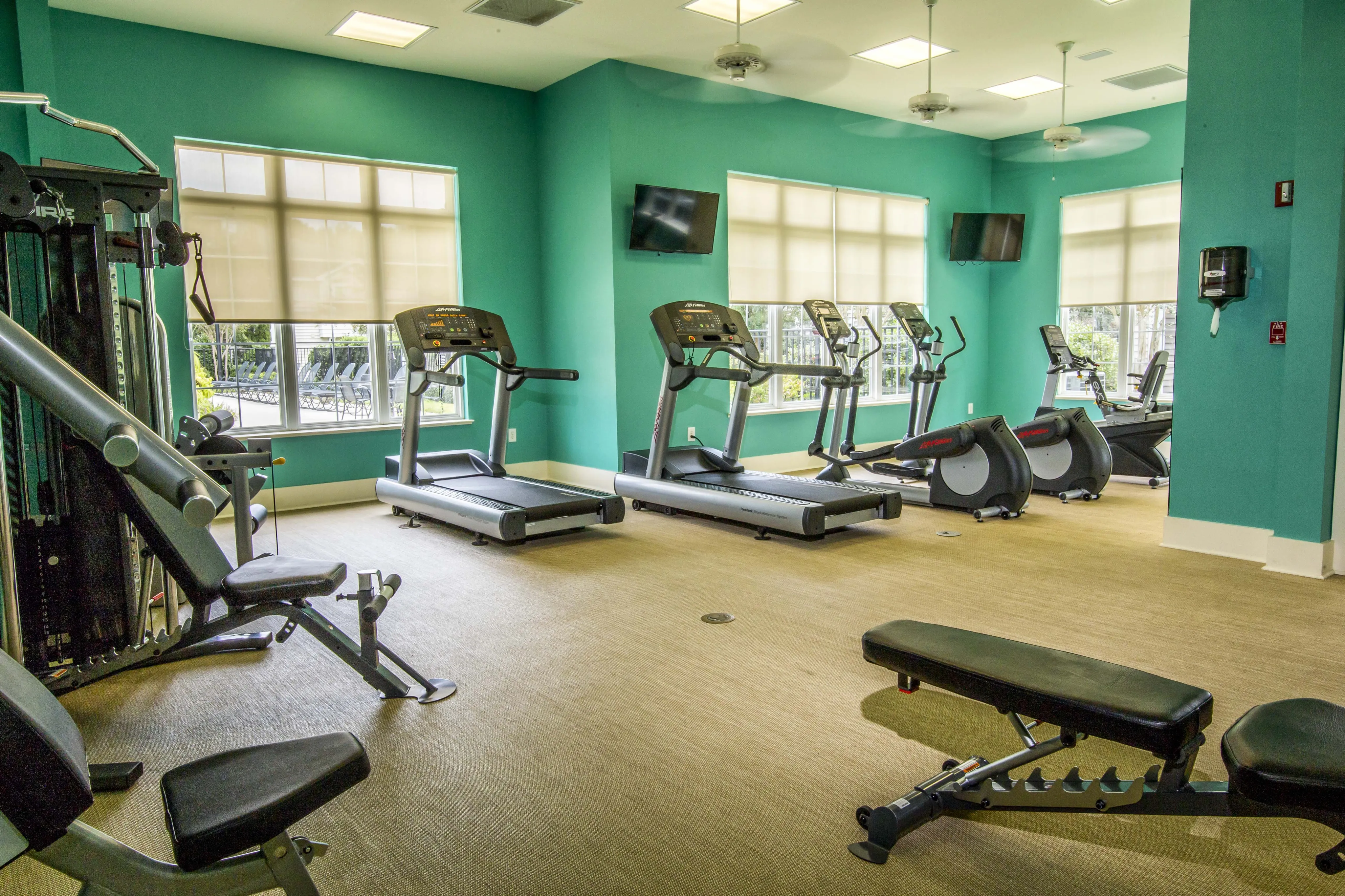 Inviting fitness center with modern treadmills, exercise bikes, and weight machines, set in a bright space with teal walls and natural light.
