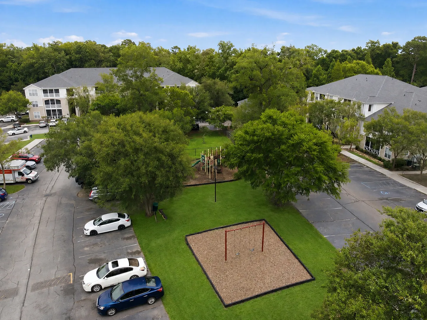 Charming apartment complex surrounded by lush greenery with modern playground and ample parking space, ideal for family living.