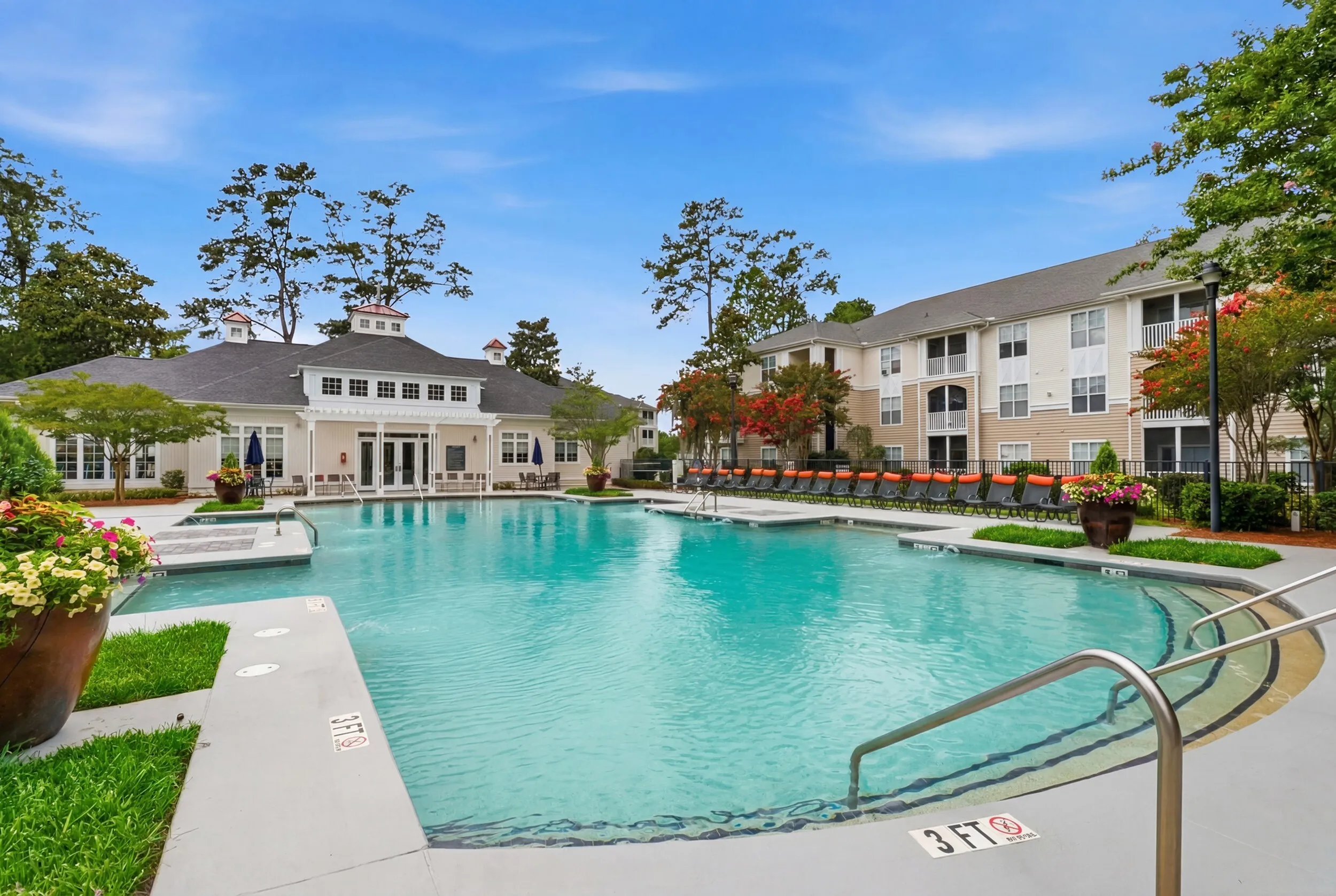 Luxurious apartment complex boasts a resort-style swimming pool with lush landscaping and a spacious sundeck equipped with vibrant orange loungers.