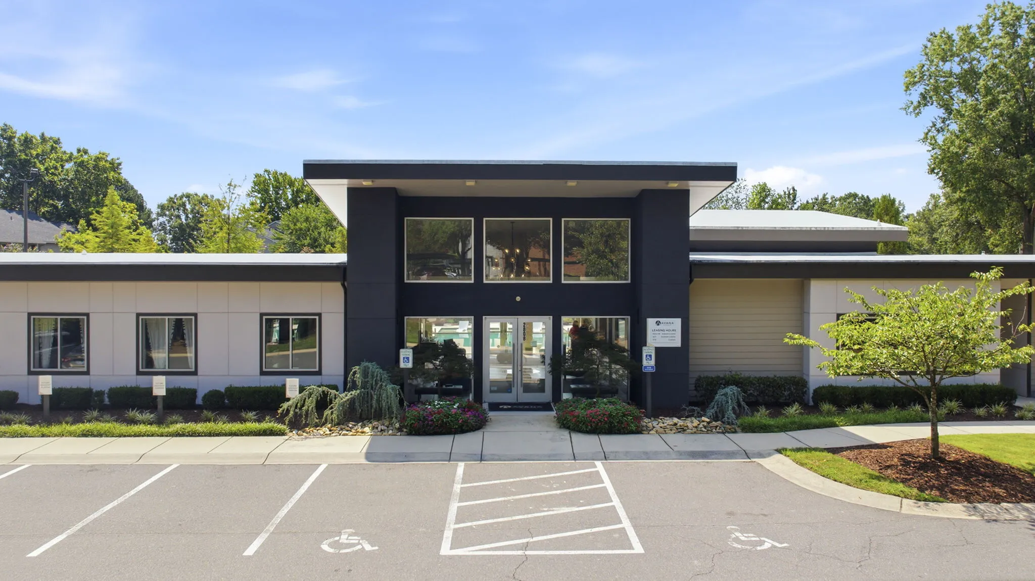 Modern building exterior surrounded by lush greenery, featuring large windows and stylish architecture.