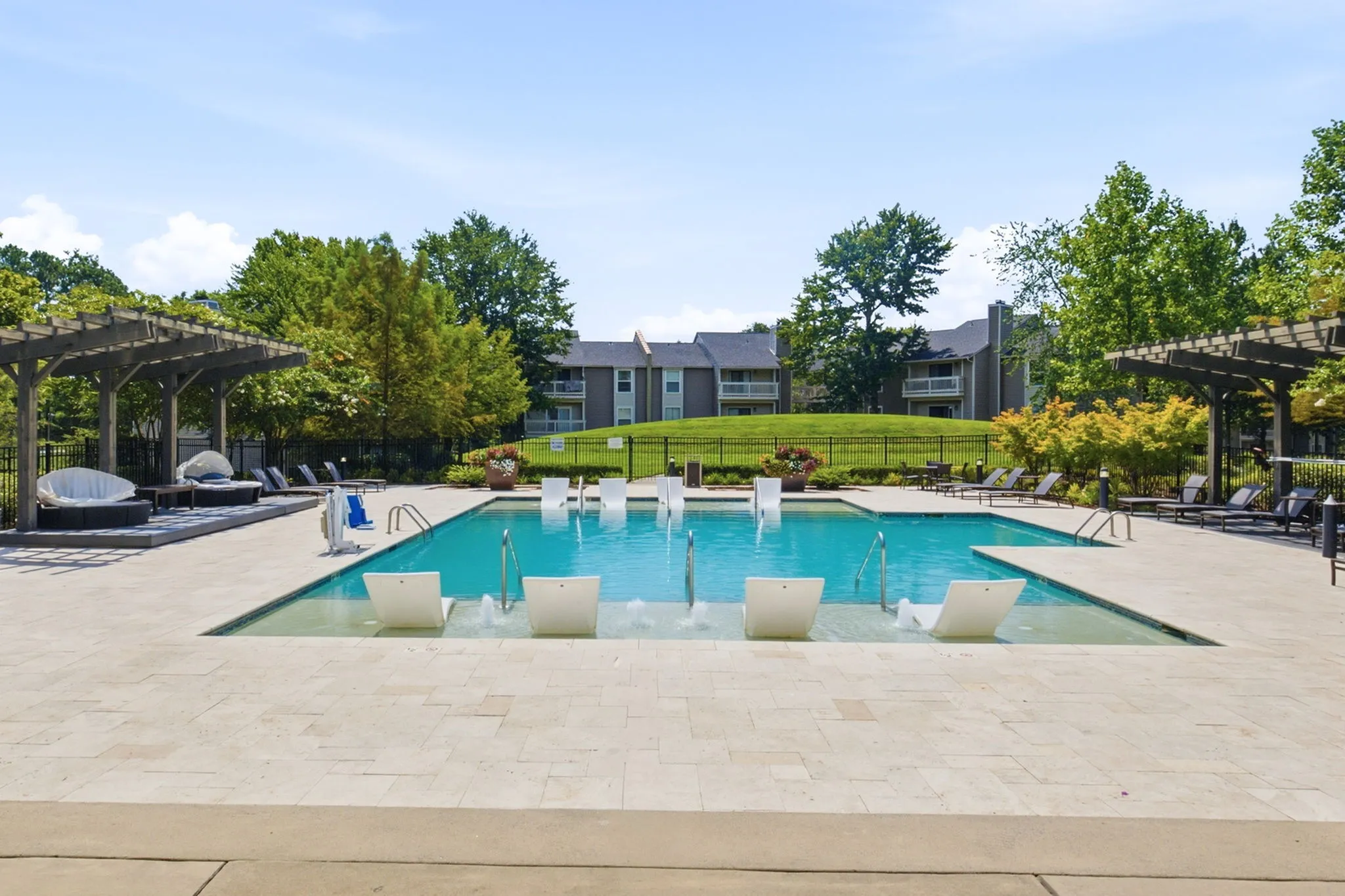 Luxurious outdoor pool area with elegant loungers, surrounded by lush greenery and stylish pergolas in a tranquil apartment complex setting.