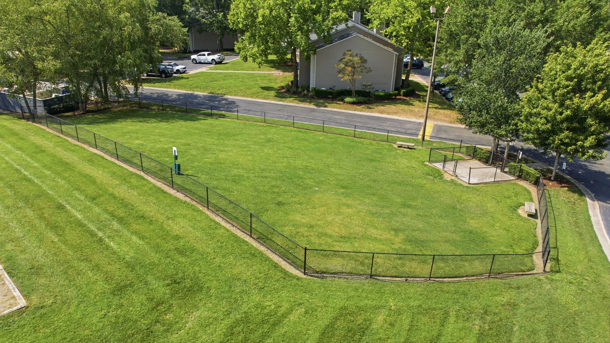 Vibrant dog park in a lush green community setting with well-maintained grass, mature trees, and easy access to nearby parking, perfect for pet owners.