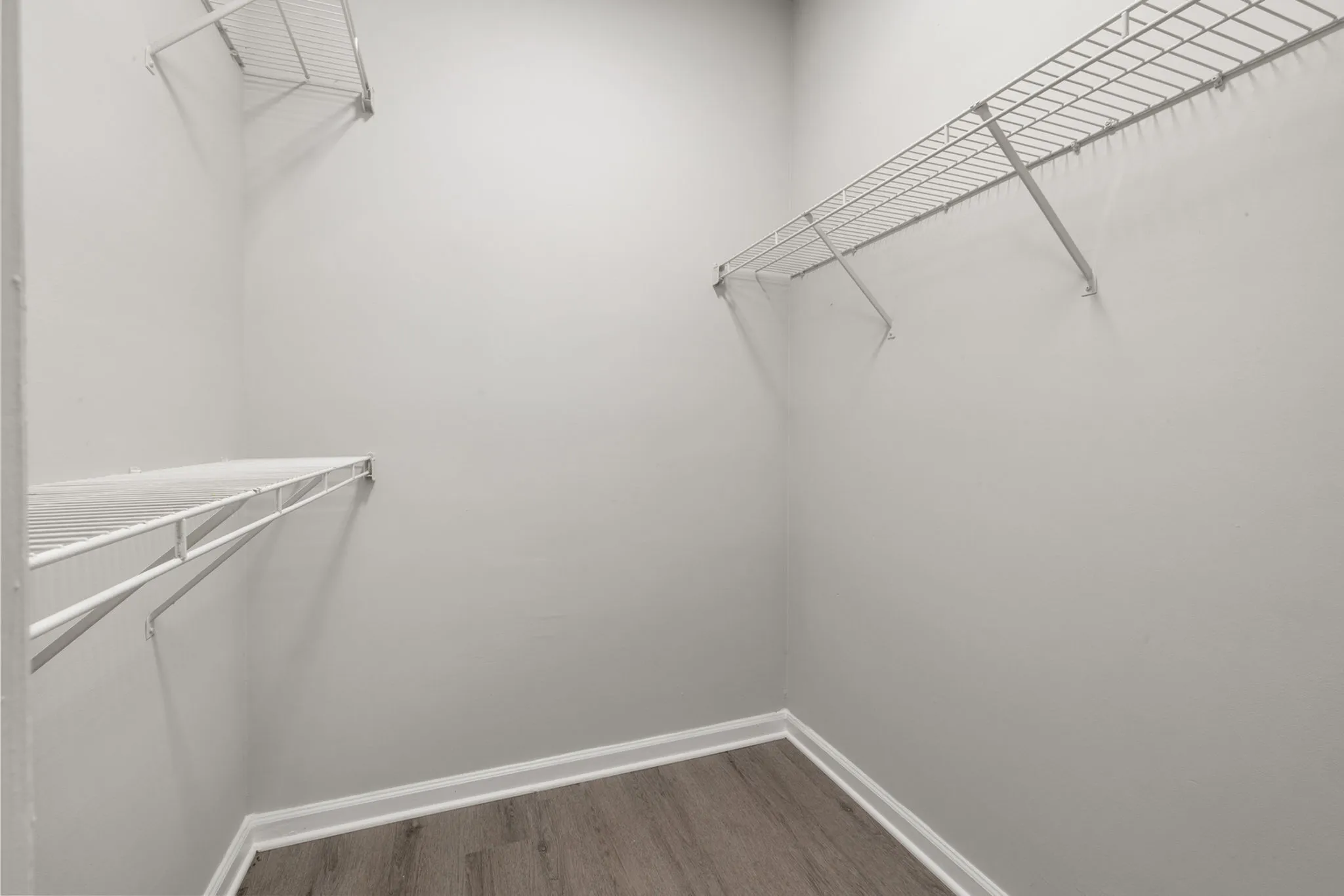 Spacious walk-in closet featuring sleek wire shelving and elegant hardwood flooring.