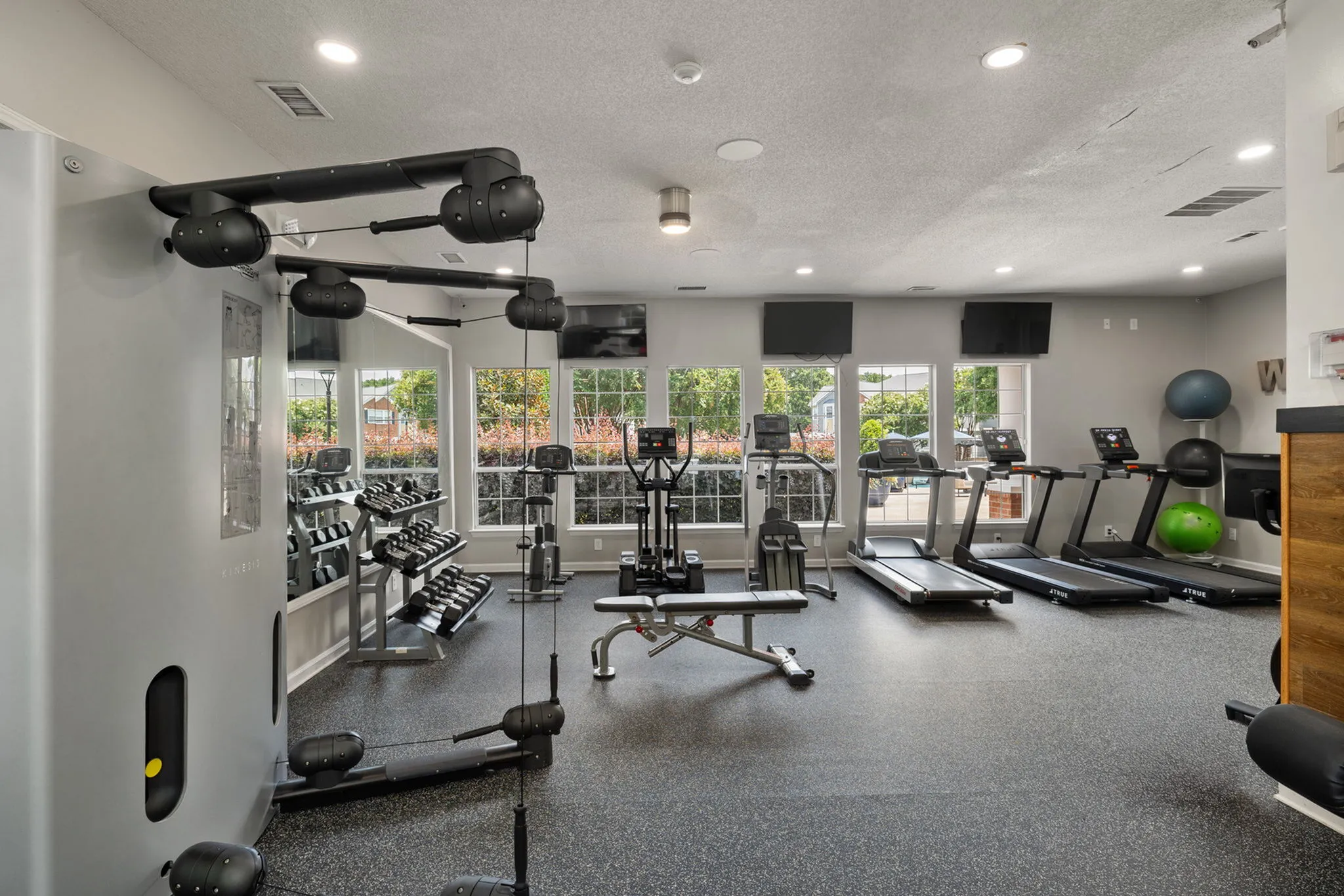 Modern apartment gym with state-of-the-art fitness equipment, cardio machines, and ample natural light from large windows.