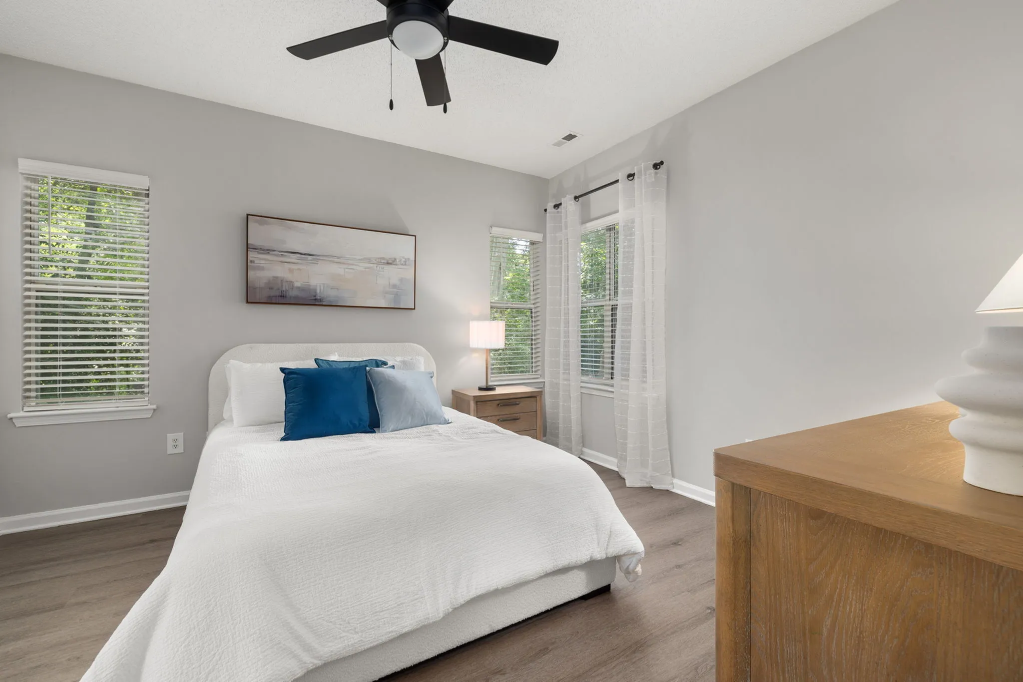 Elegant bedroom featuring a cozy bed with blue cushions, ambient lighting, and modern decor, complemented by large windows with serene garden views.