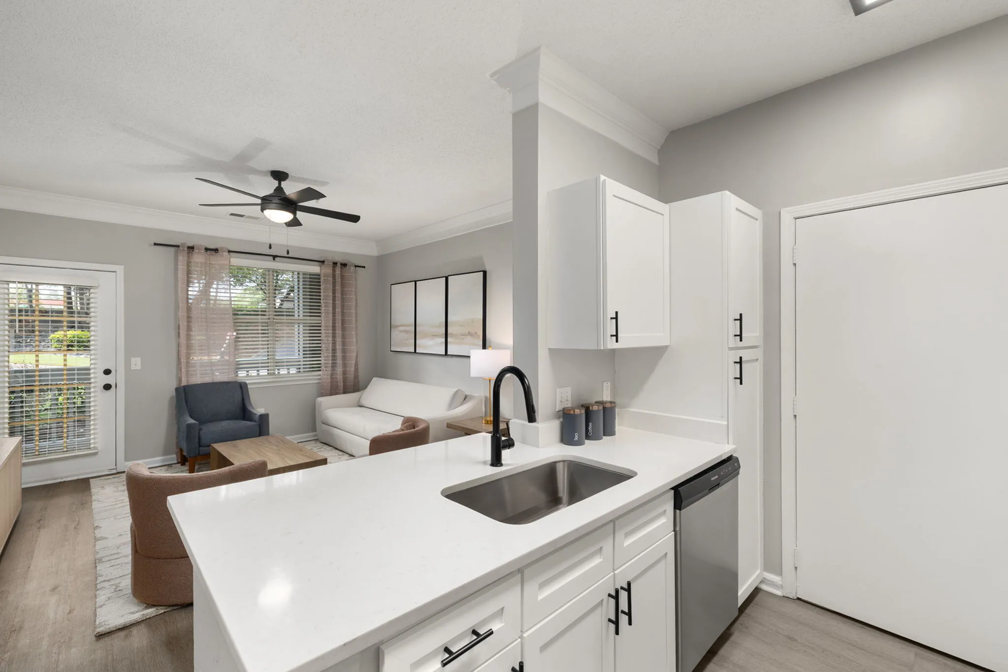Modern apartment interior with an open kitchen layout, elegant white cabinetry, and a cozy living area featuring a stylish white couch and armchairs for comfortable seating.