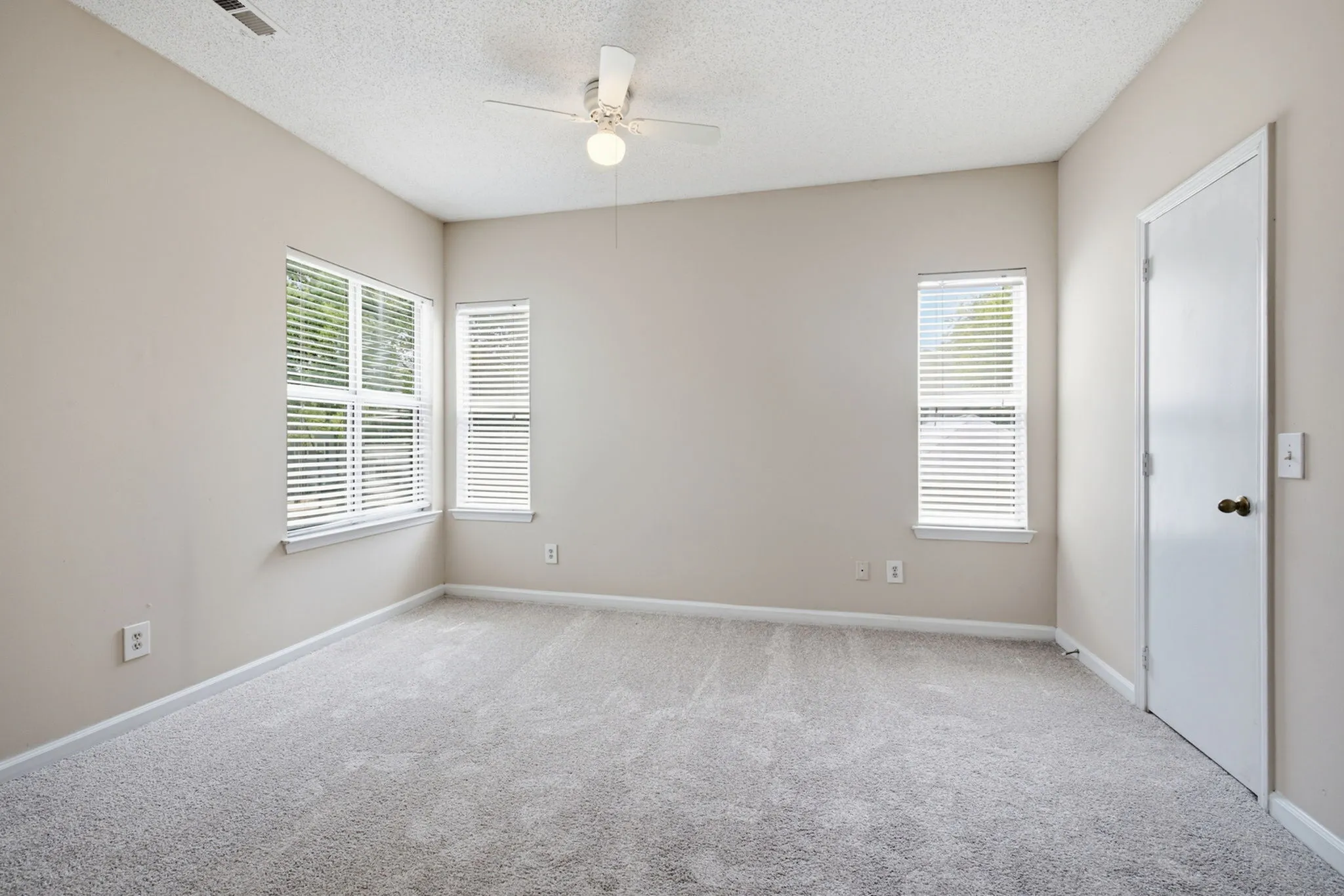 Bright, inviting bedroom with plush carpeting, neutral walls, and ample natural light from multiple windows.
