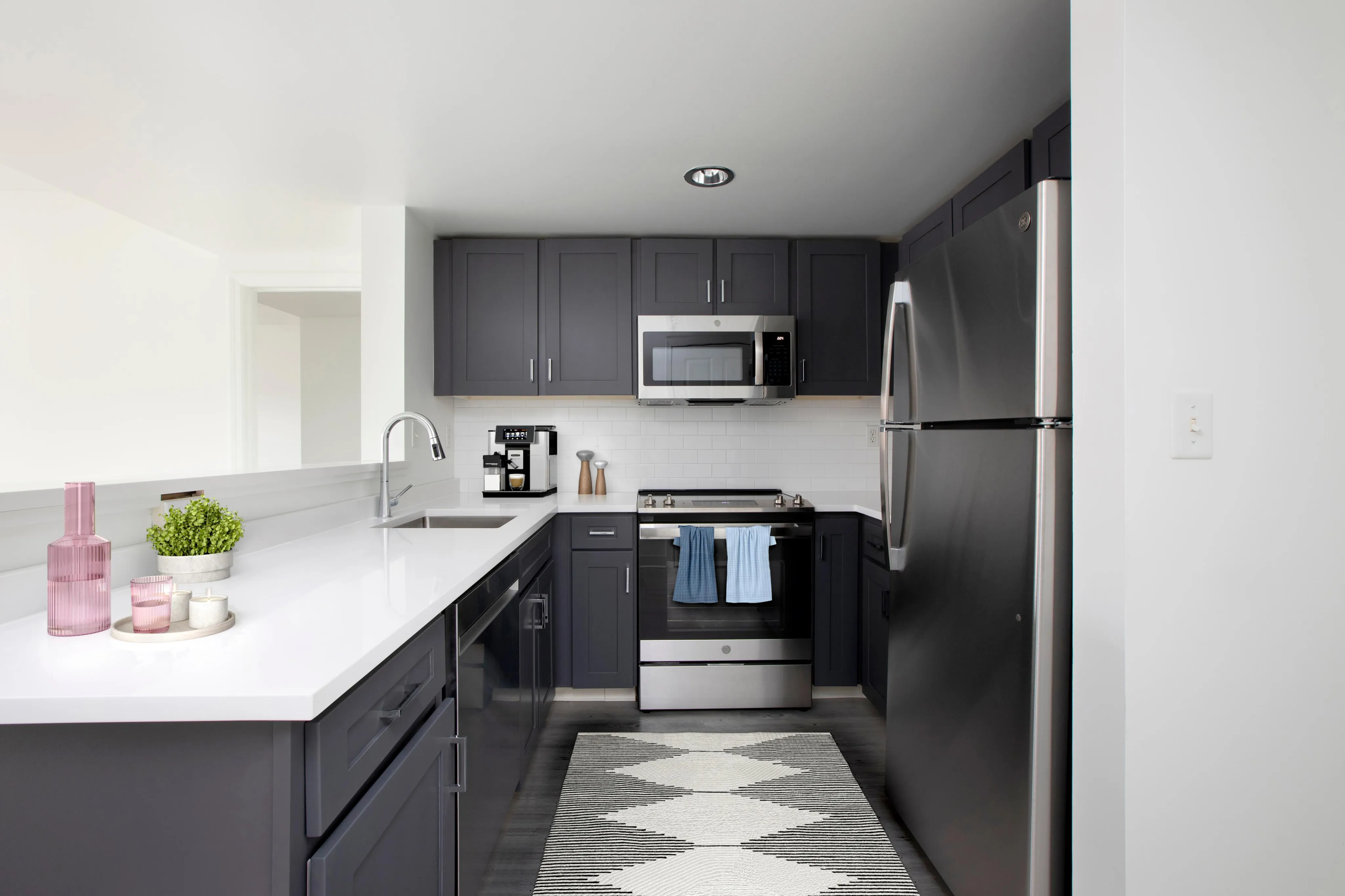 Contemporary kitchen with sleek dark cabinets, stainless steel appliances, and a spacious white countertop accented by stylish decor.