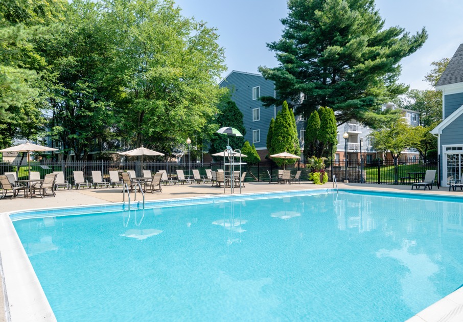 The pool area at our apartments for rent in Germantown, MD, featuring beach chairs, umbrellas, and outdoor furniture.