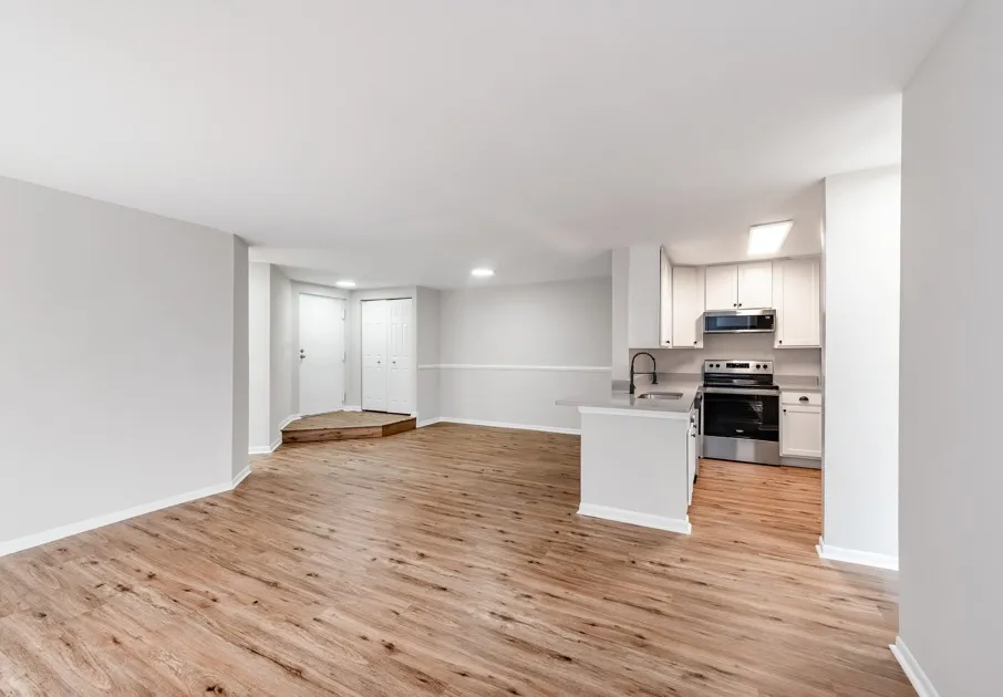 Empty living room at our apartments for rent in Germantown, featuring wood grain floor paneling and a view of the kitchen.