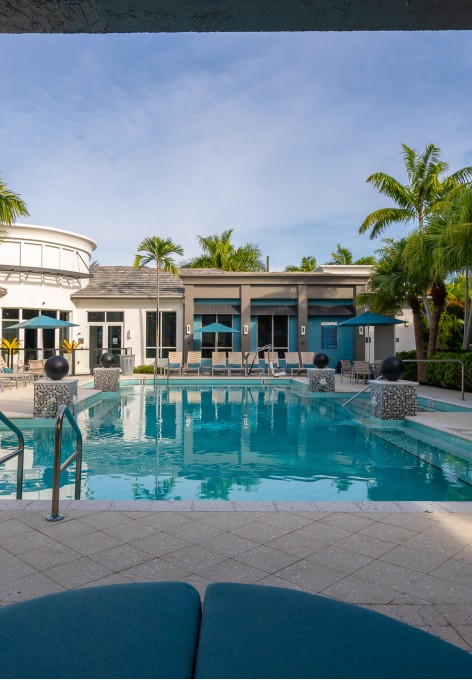 Outdoor swimming pool at our Delray Beach apartments for rent, featuring lounge chairs and palm trees.