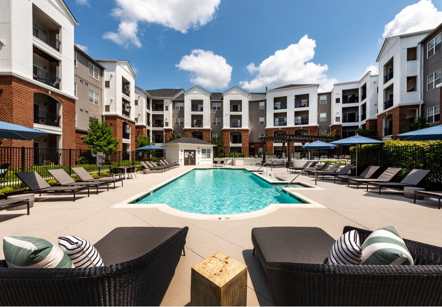 The pool area at our apartments for rent in Herndon, VA, featuring beach chairs, umbrellas, and a view of the apartments.