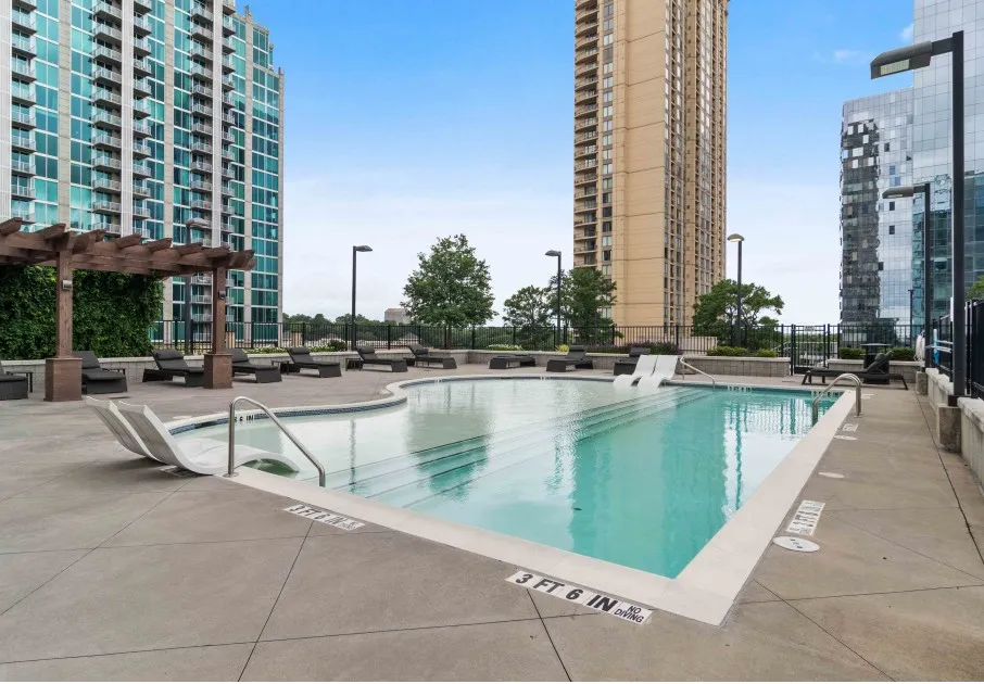 Outdoor pool area at our apartments featuring outdoor reclining chairs, a shade structure, and pool chairs.