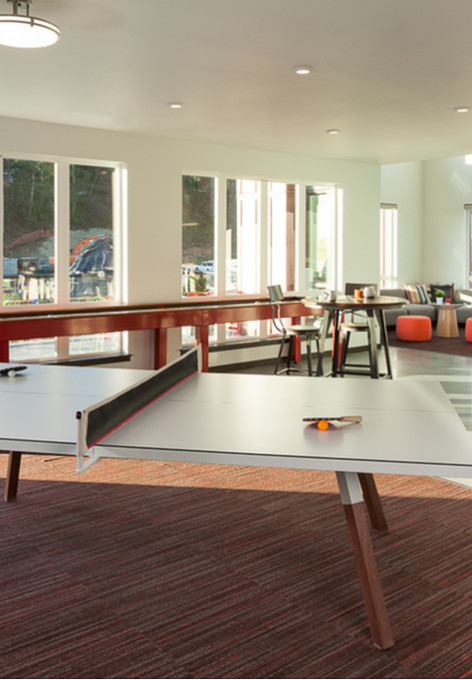 Model living room at our apartments for rent in Kenmore, WA, featuring a recreational ping pong table and large windows.