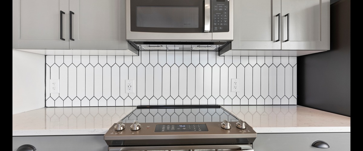 Detail of a model kitchen at Beckon Apartments for rent in Durham, NC, featuring an electric range and tiled backsplash.