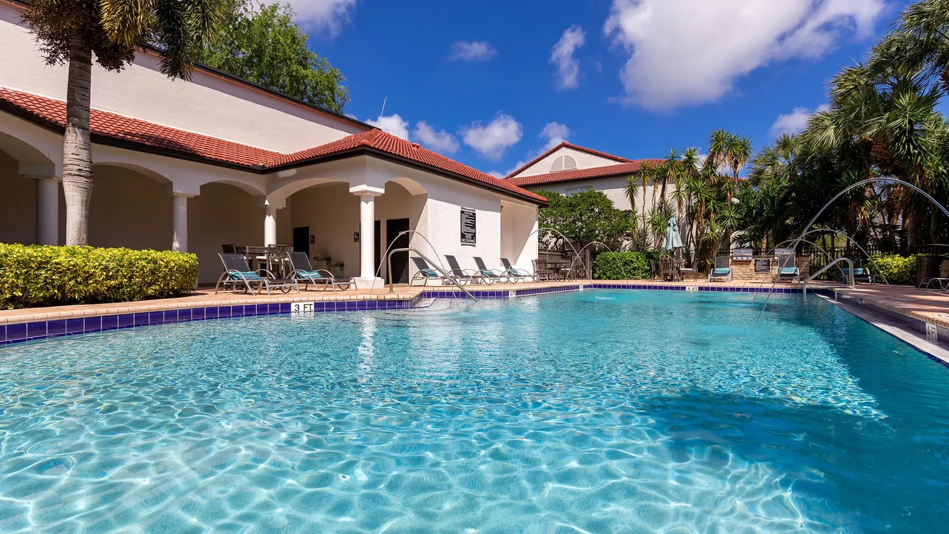Outdoor swimming pool at our luxury apartments for rent in West Palm Beach, FL, featuring lounge chairs and palm trees.