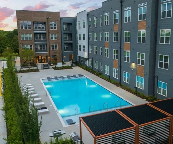 The pool area at Flats at General Time Apartments in Athens, GA, featuring lounge chairs and the sky at dusk.