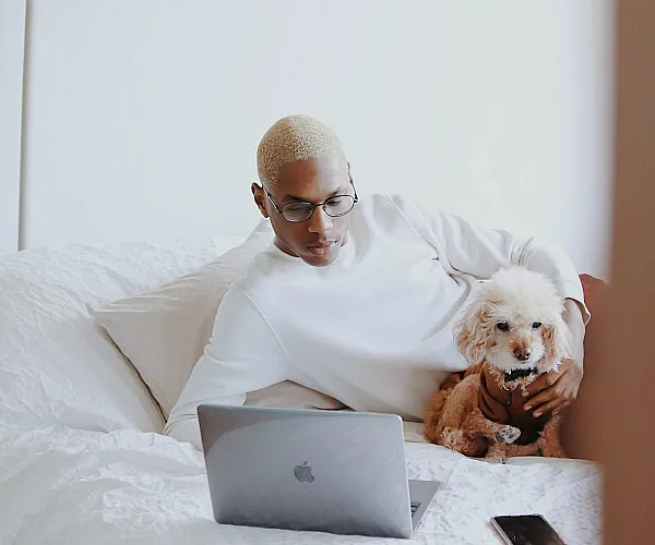 person on bed with dog and computer
