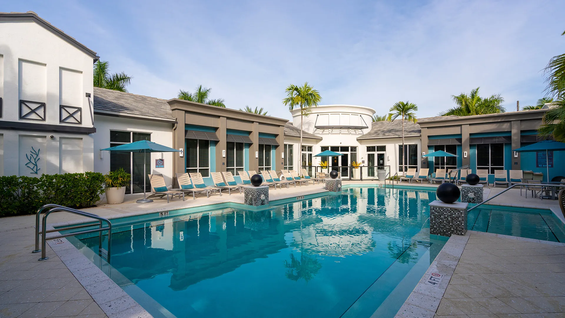 Luxurious apartment complex featuring a pristine outdoor pool, surrounded by modern architecture and lush palm trees, offering a tropical oasis experience.