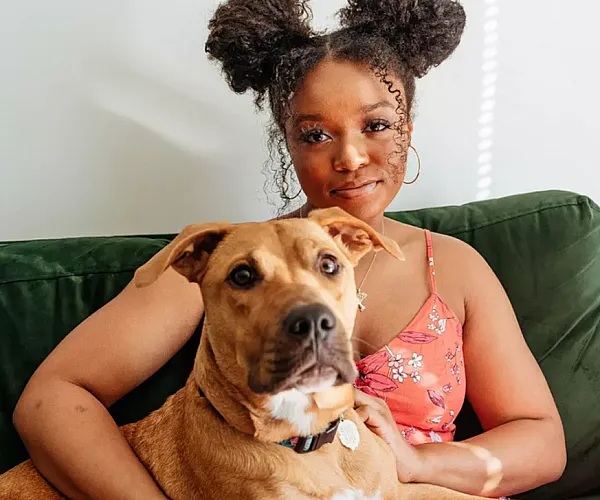 Bright and cozy living room setting with a person in a floral dress enjoying a relaxing moment on a green couch with their friendly dog.