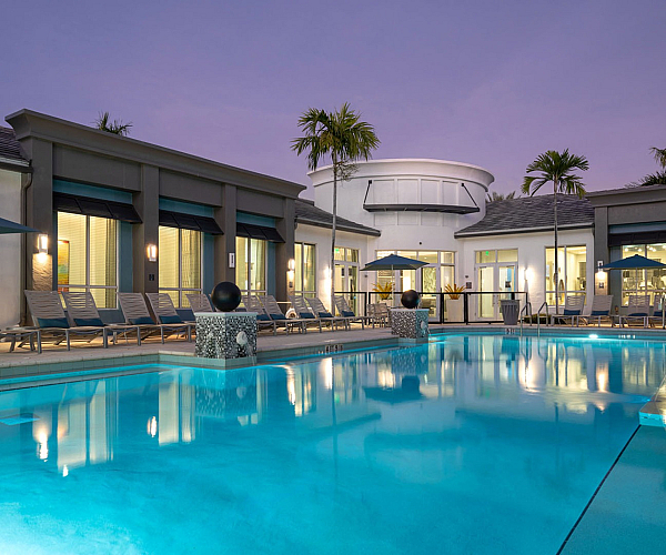 Luxurious resort-style pool with modern design, surrounded by elegant loungers and palm trees at sunset.